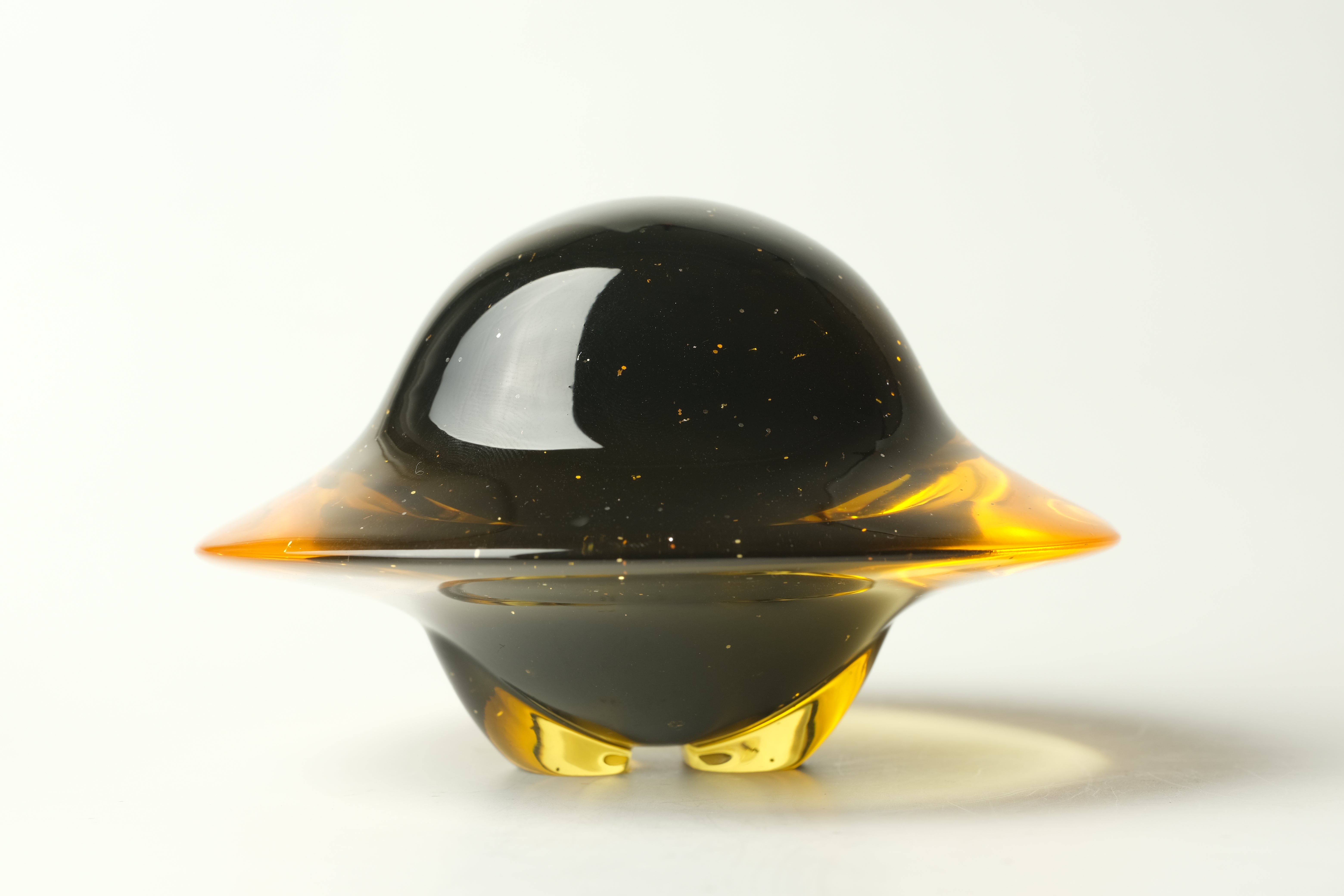 Darkmite by Yutoos: A 3.5 unique, spherical art-glass sculpture with black and gold flecks, featuring translucent amber-gold sections, creating a floating, UFO-like appearance.