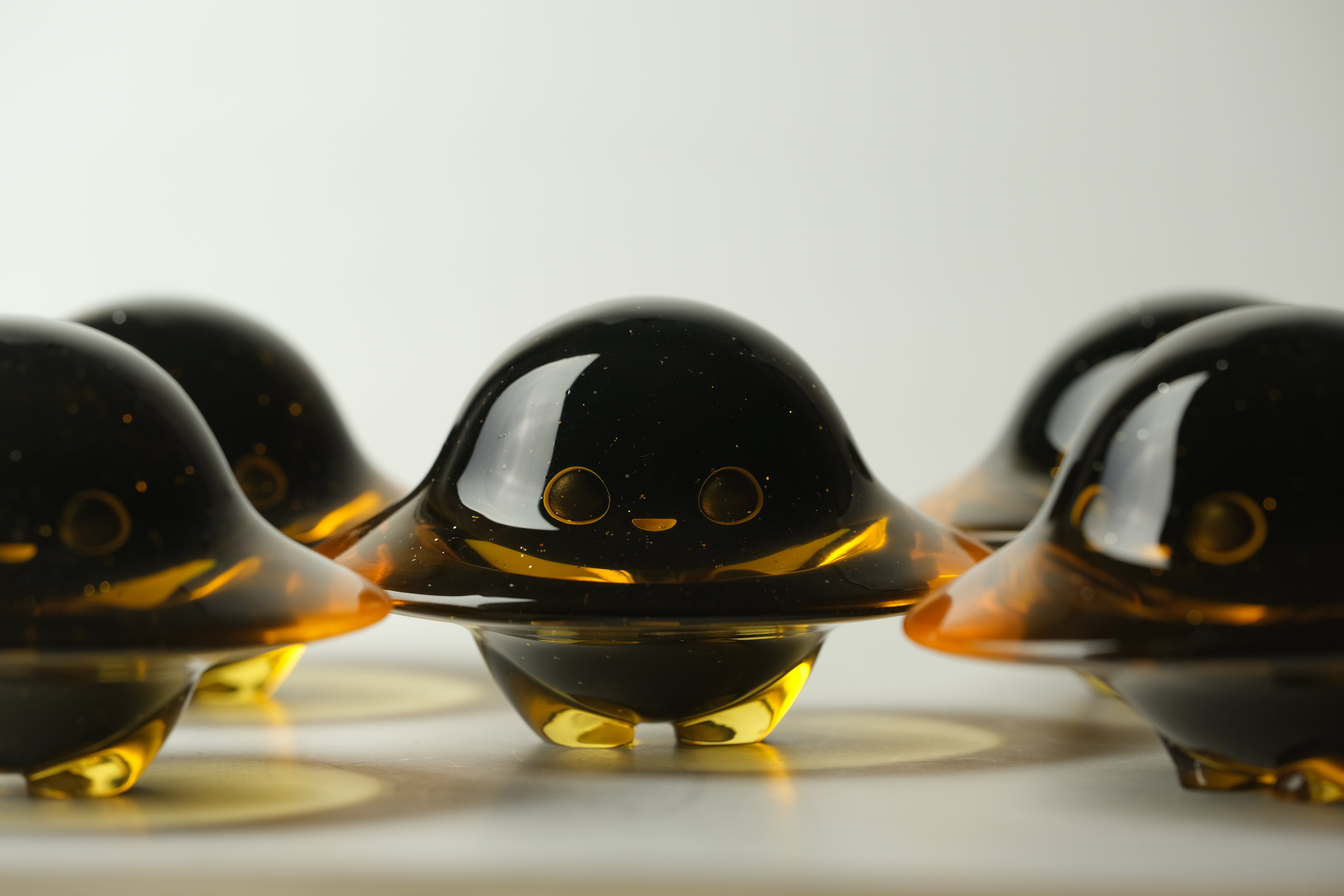 Darkmite by Yutoos: Cluster of small, amber resin figurines with domed hats, round eyes, and stubby feet, each uniquely crafted, 3.5 inches tall. Edition of 50.