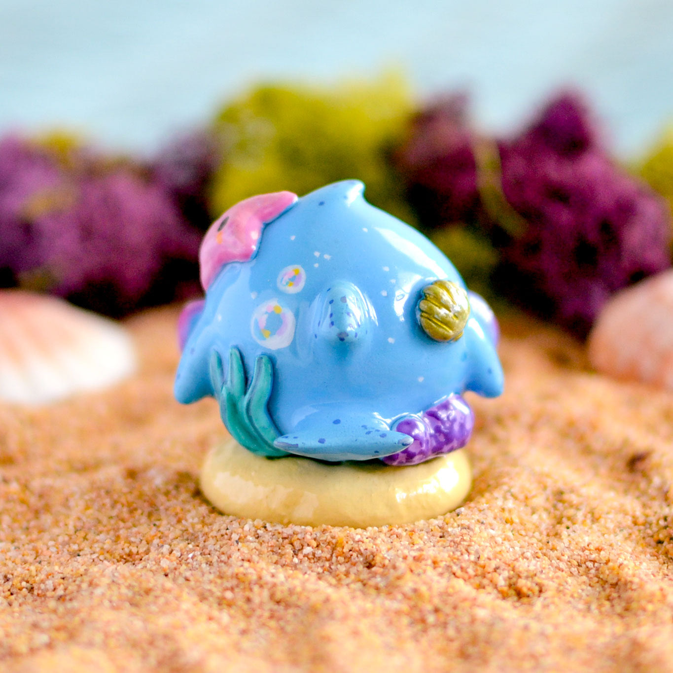 Little Shit Bigger Deal - Beasties Bites by Dear Beasties x Trash Panda: Close-up of a miniature blue fish figurine on sand, 1.5 collectible art toy.