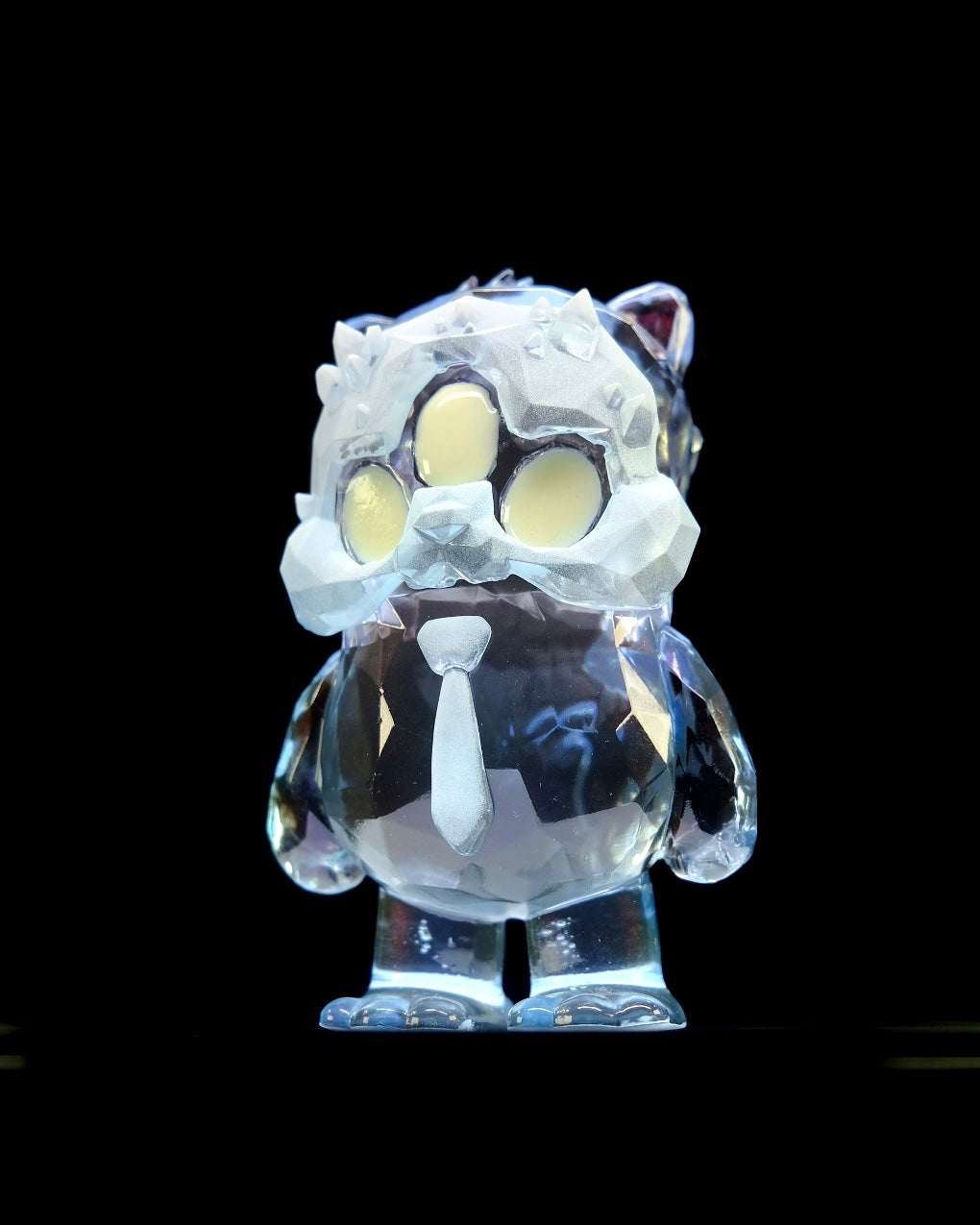 Beans Group Show - Arctic Beans by DTC Studios x Josh Divine: A 5 faceted crystal-like resin figurine, owl-cat shaped, with frosted ice mask and necktie, glowing against black. Preorder.