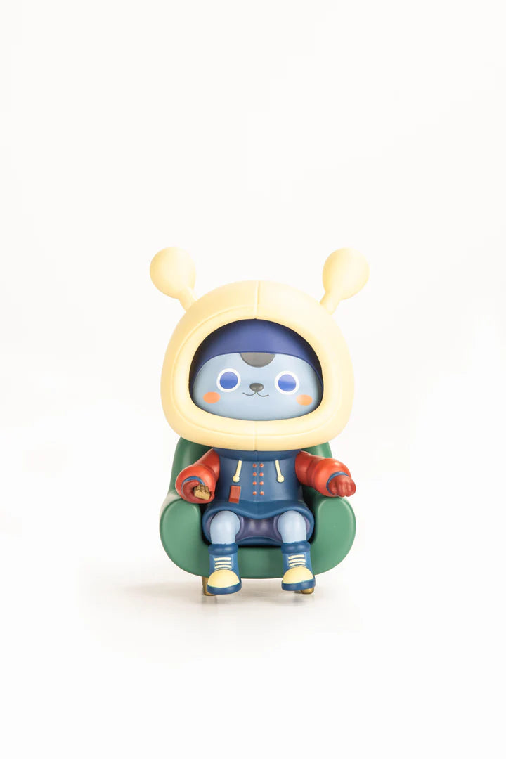 Vinyl figure Napa Series One seated in green armchair, wearing yellow hood, blue hoodie, and holding a remote, part of Strangecat Toys' limited edition collectibles.