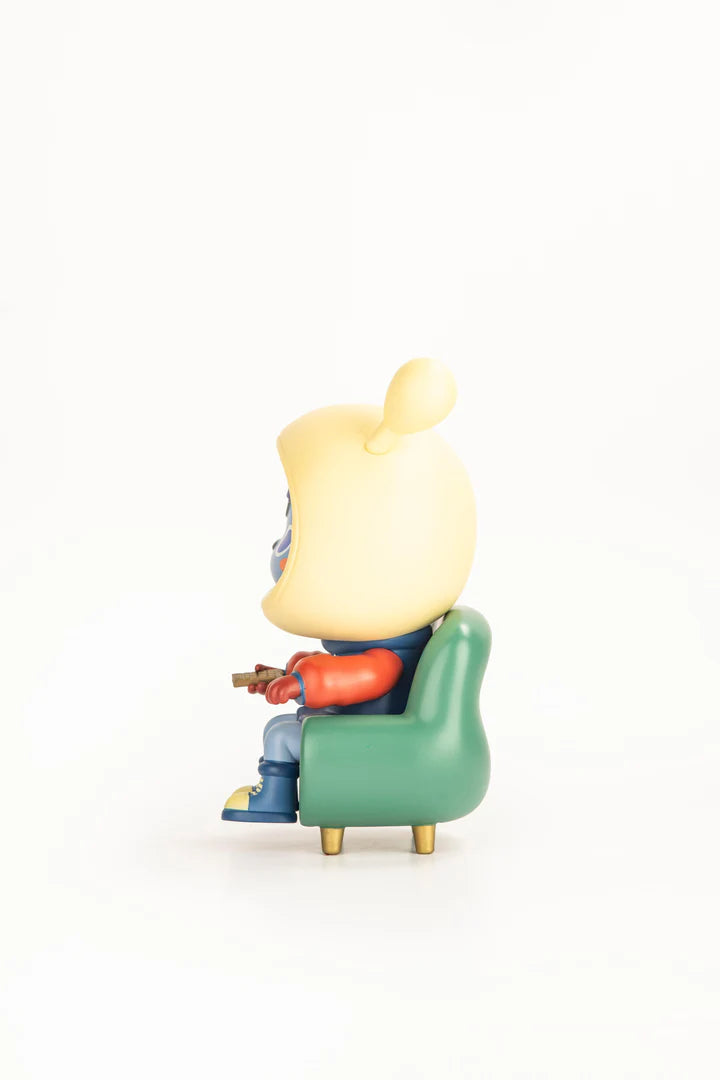 Napa Series One figurine in a green armchair, wearing a yellow helmet and red jacket, holding a controller. Limited edition collectible from Strangecat Toys.