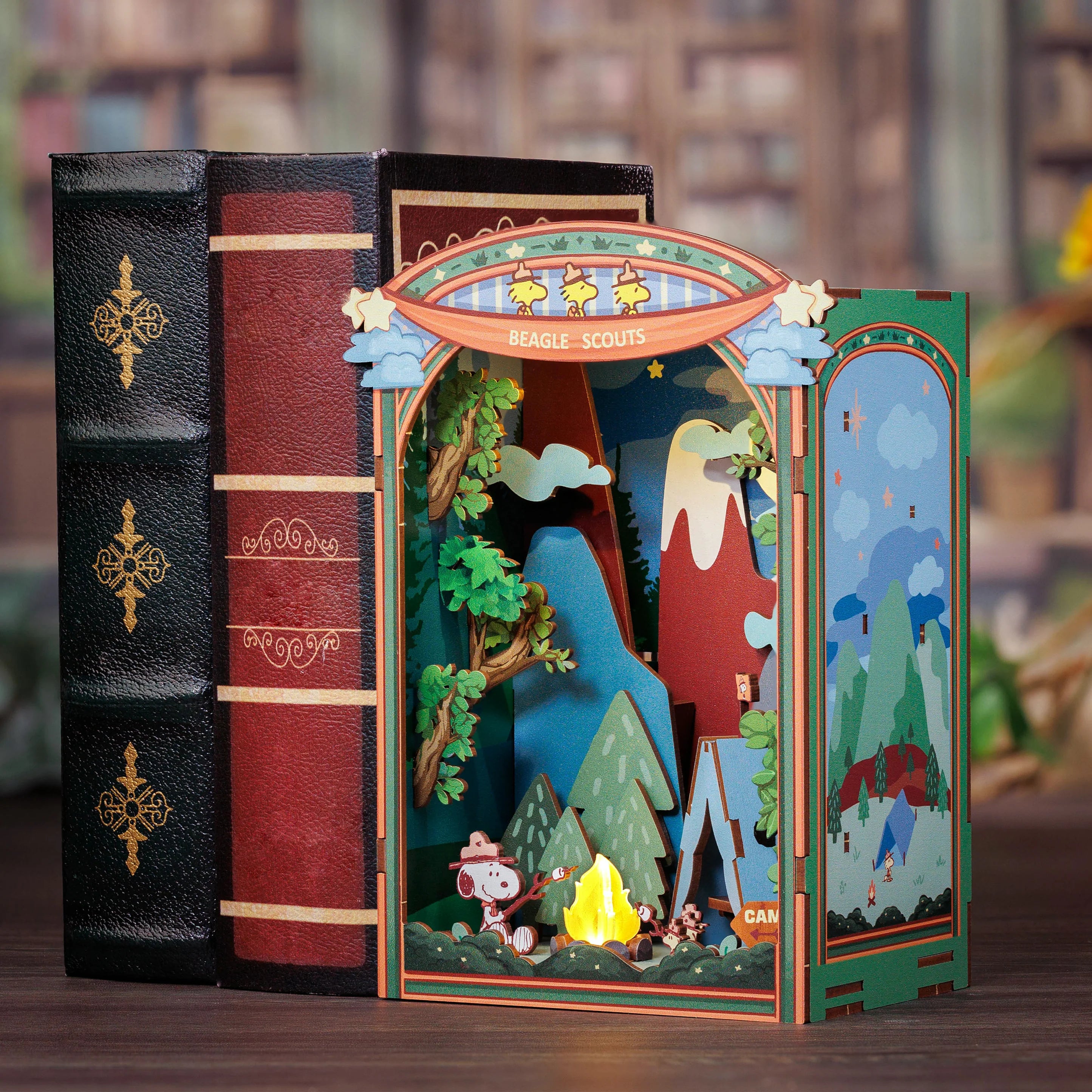 Peanuts® Snoopy’s Beagle Scouts diorama; Snoopy toasts marshmallows by a campfire, surrounded by trees, tent, and mountains, styled as an open book.