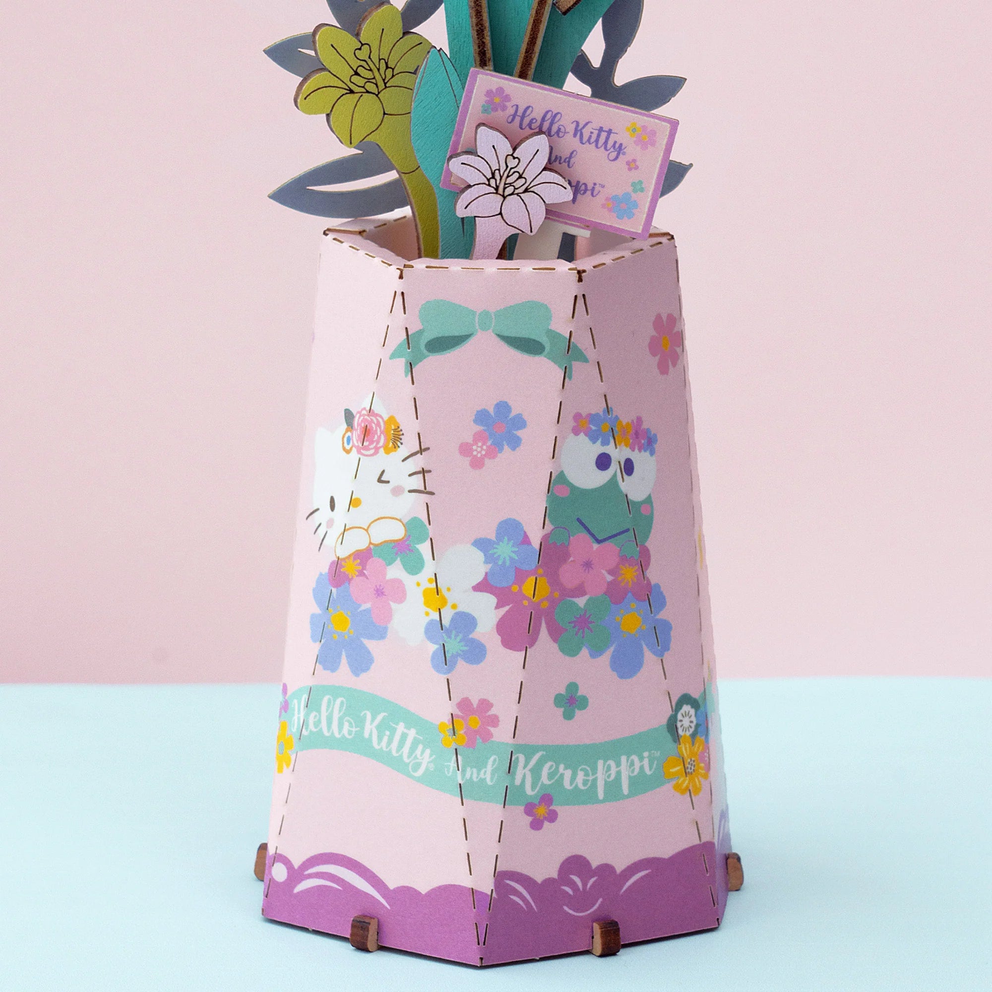 Hello Kitty® and Friends Keroppi and Hello Kitty Lily DIY puzzle kit features a pastel-pink hexagonal paper vase adorned with character cutouts and paper flowers.