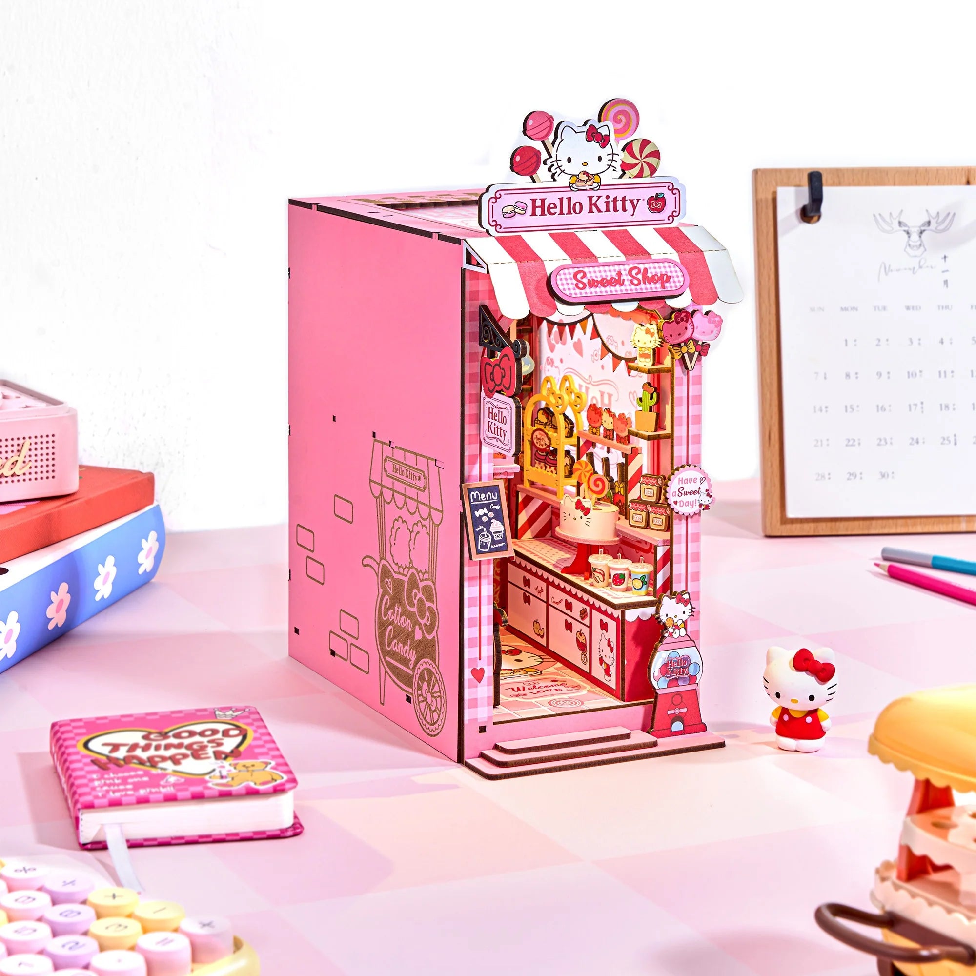 Hello Kitty® Sweet Shop Booknook diorama with candy-themed decor, featuring Hello Kitty figurine, notebook, and accessories on a pink, checker-patterned tabletop.