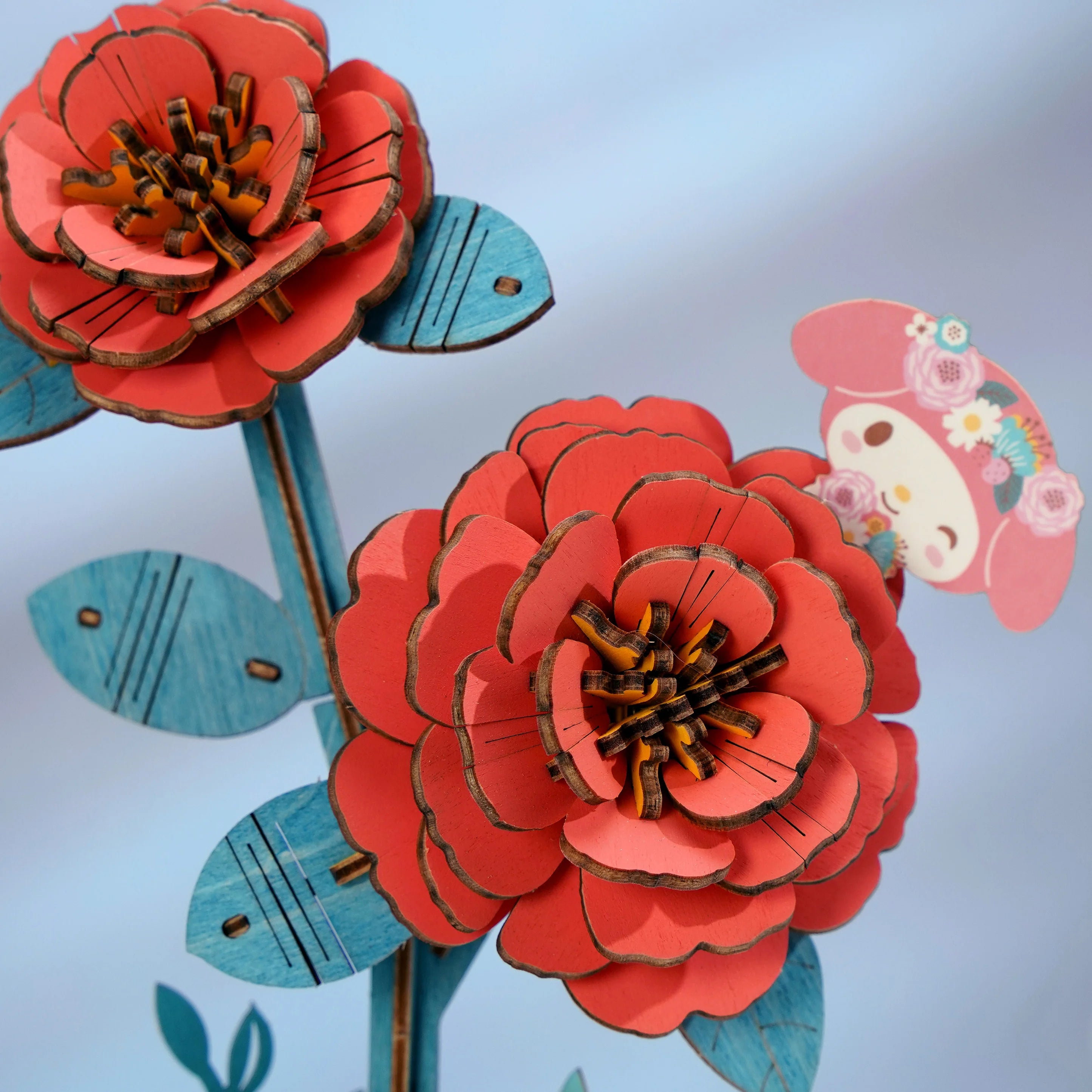 Hello Kitty® and Friends My Melody Red Camellia 3D wooden puzzle bouquet, featuring coral-red blooms and turquoise-blue stems, with a cute floral-crowned character tag.