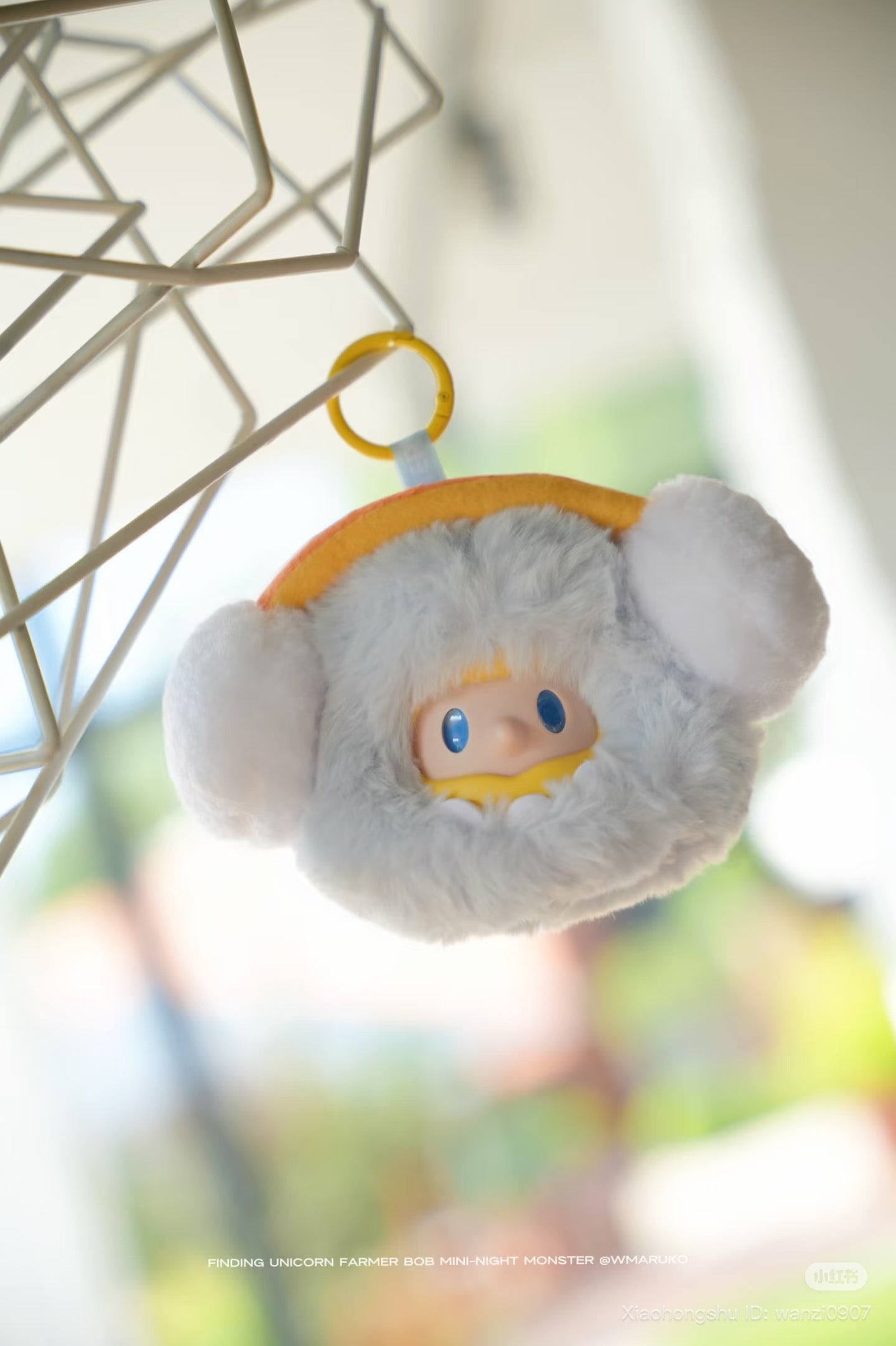 Farmer BOB MINI-NIGHT Monster Blind Box Plush Keychain, featuring a fluffy gray monster with earmuff tufts and a yellow-hooded face, hanging by a yellow ring.