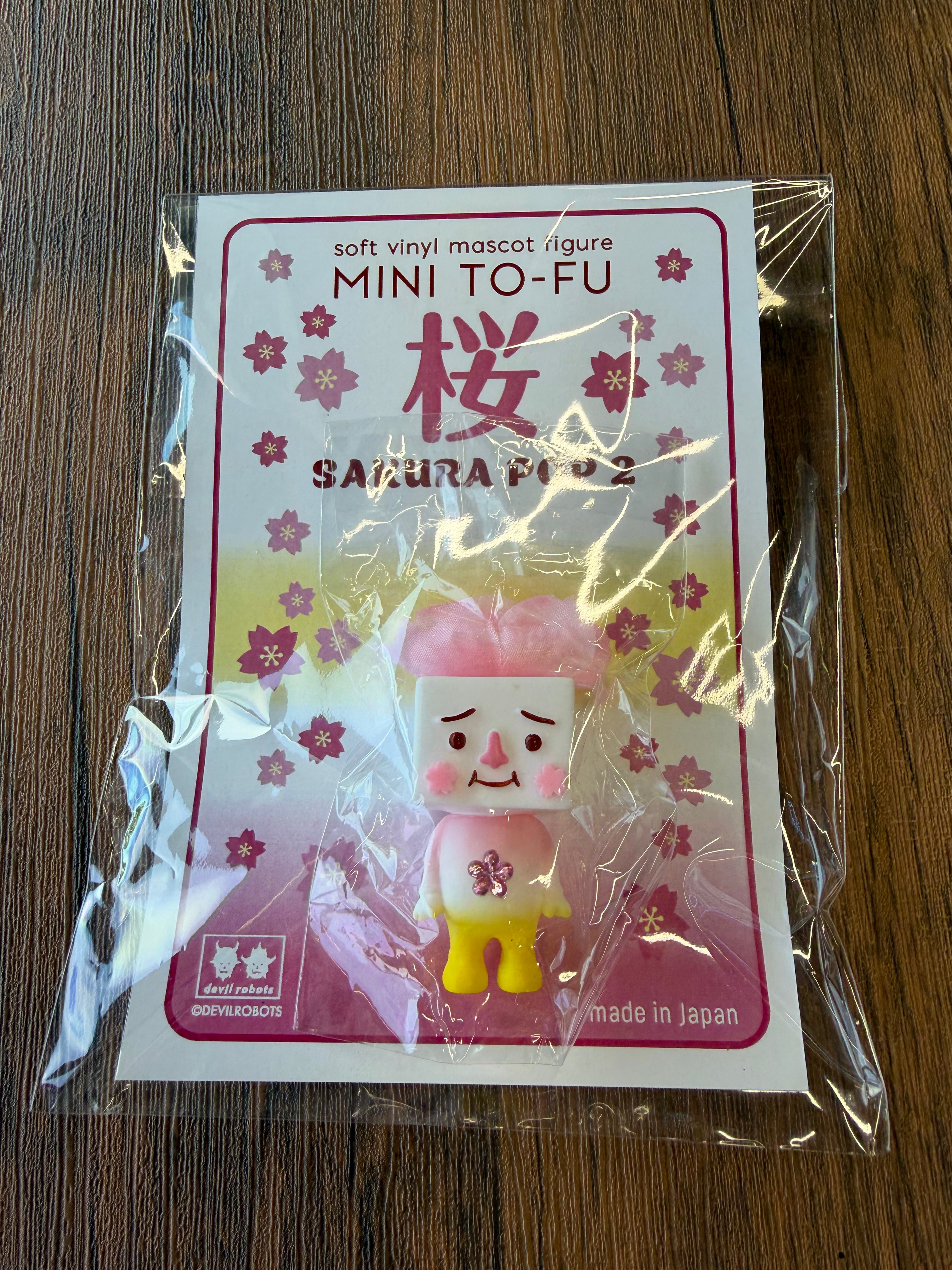 Mini To-fu - Sakura Pop by Devilrobots: A 5cm sofubi vinyl figure with tofu-shaped head, cherry-blossom accents, and flower decal, sealed in retail packaging.