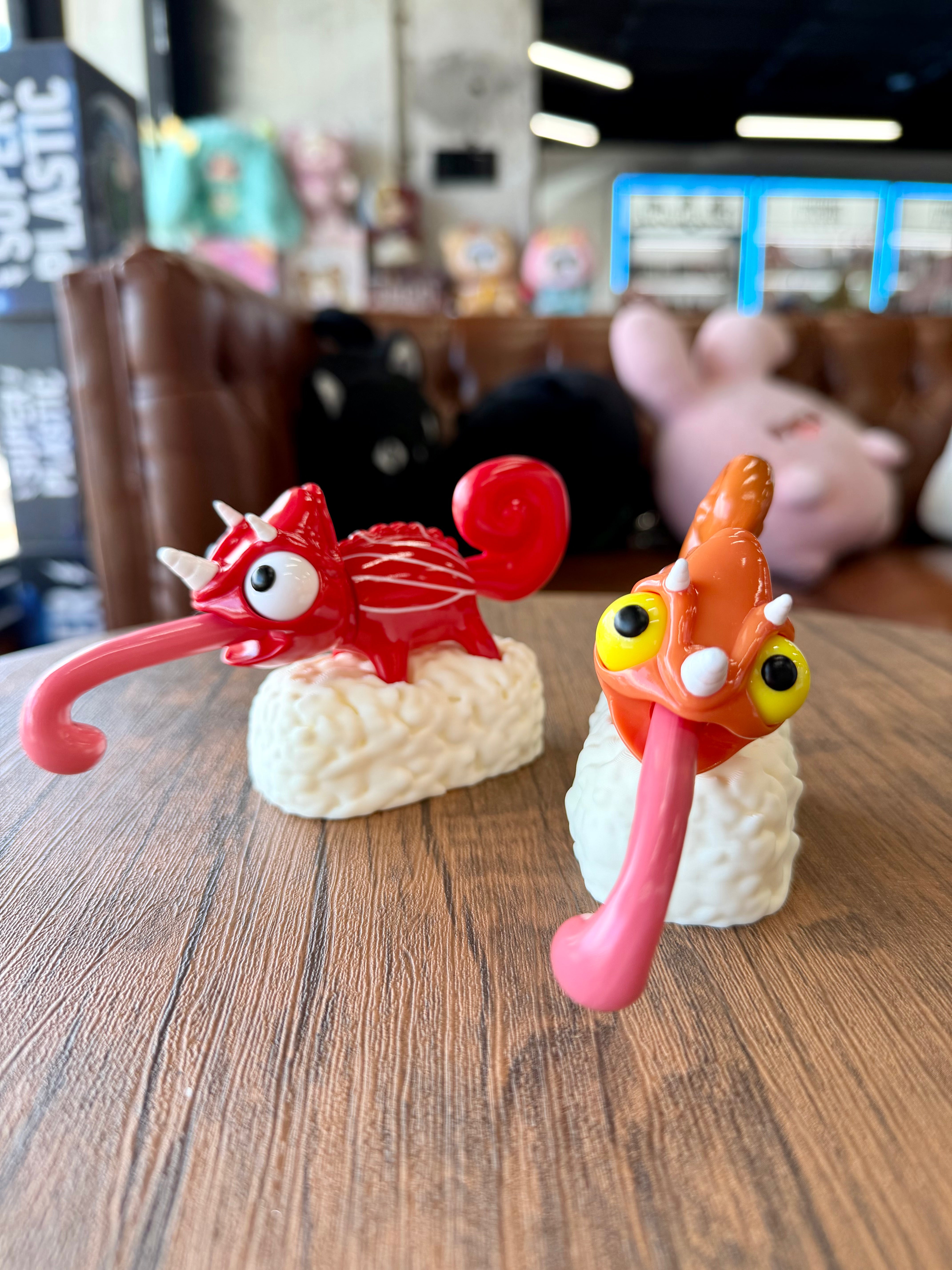 Two soft vinyl Sushi Gogo Chameleon figures, each a whimsical reptile topping a sushi base, displayed on a tabletop.