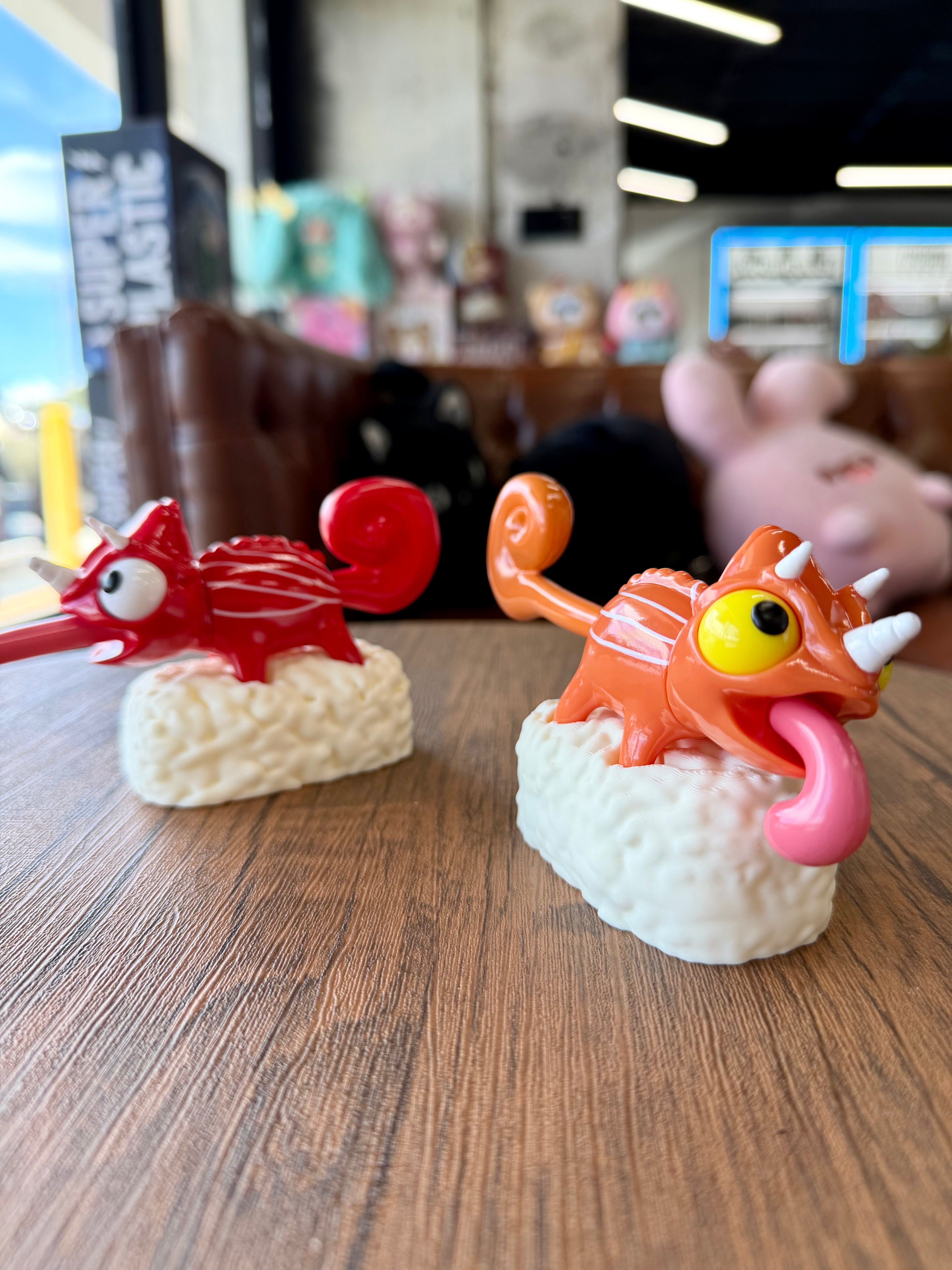 Sushi Gogo Chameleon figures on rice blocks, featuring quirky chameleon designs with curled tails and bulging eyes, displayed on a wooden tabletop.