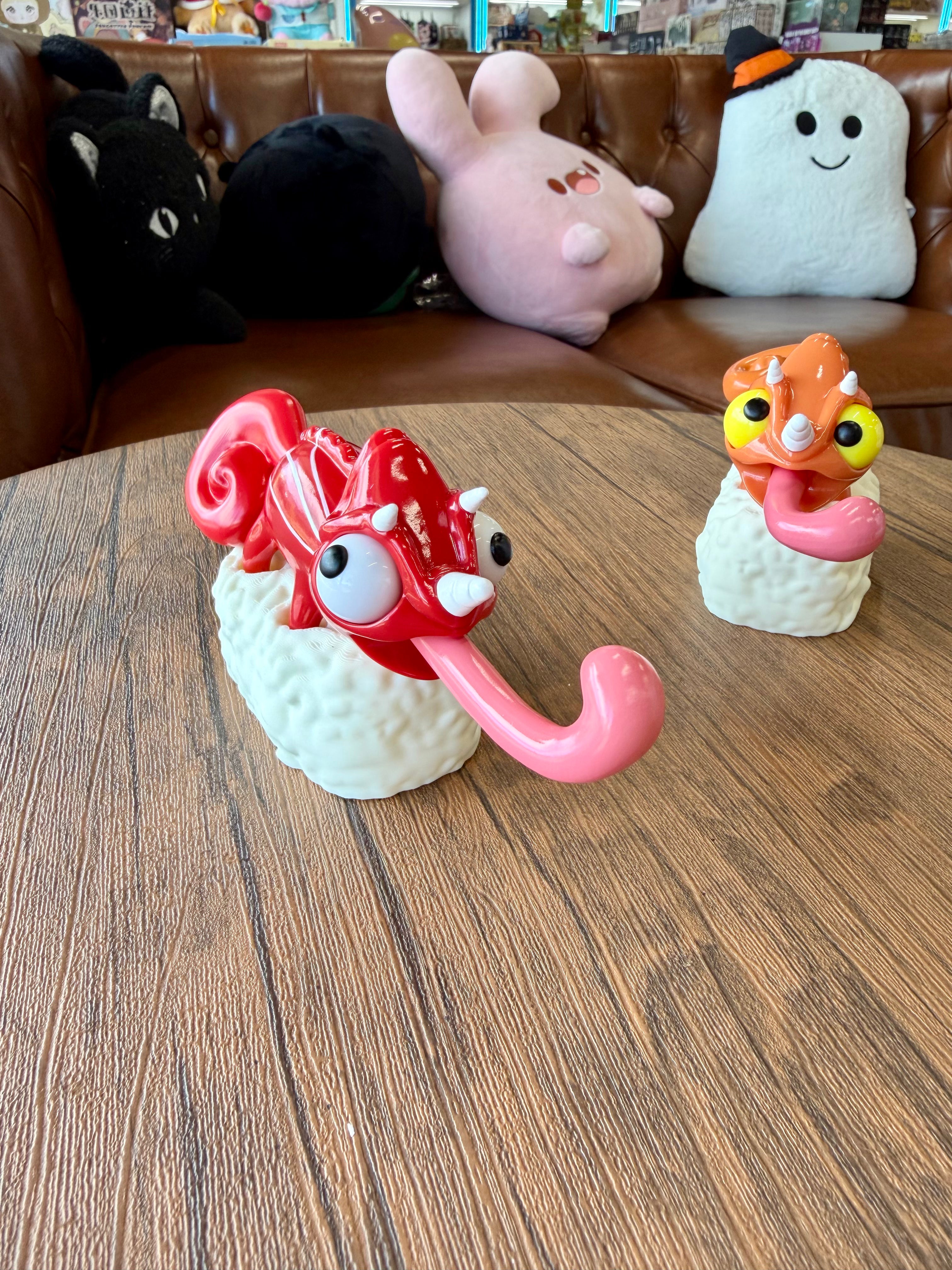 Sushi Gogo Chameleon toy sculptures on display, each perched on sushi rice, with oversized eyes and long tongues, embodying Strangecat Toys' whimsical art collection.