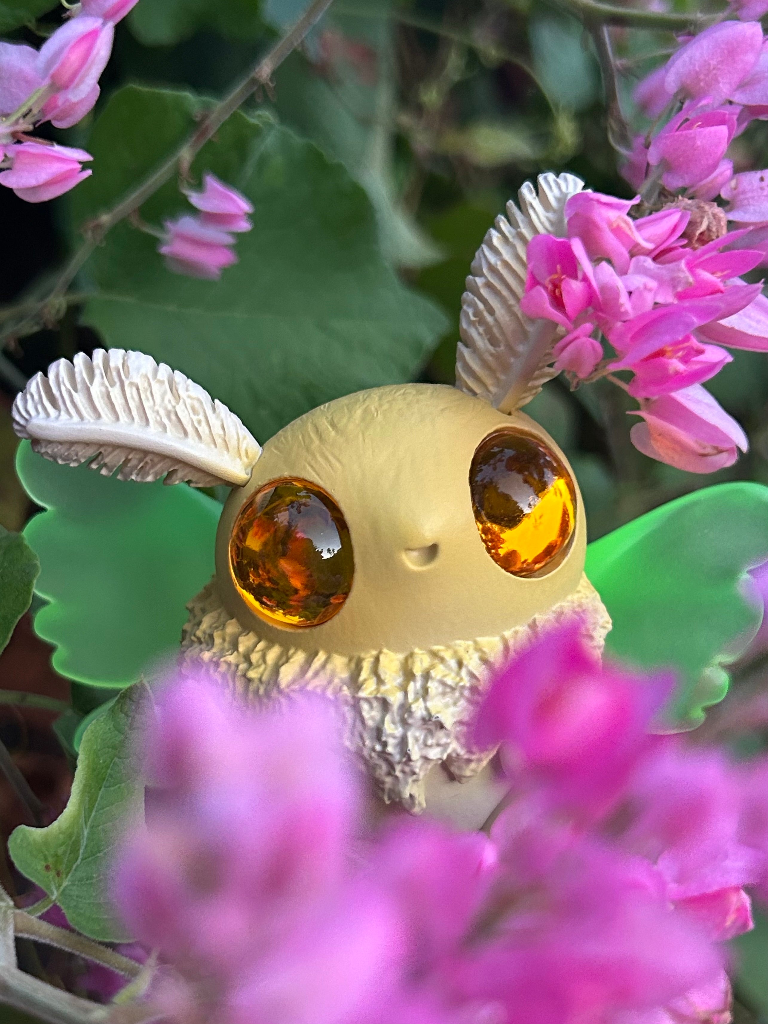 Cryptkid - Luna Mothman by Hazel Owlery, a whimsical toy with large eyes and wings, surrounded by pink flowers, perfect for collectors of unique art toys.