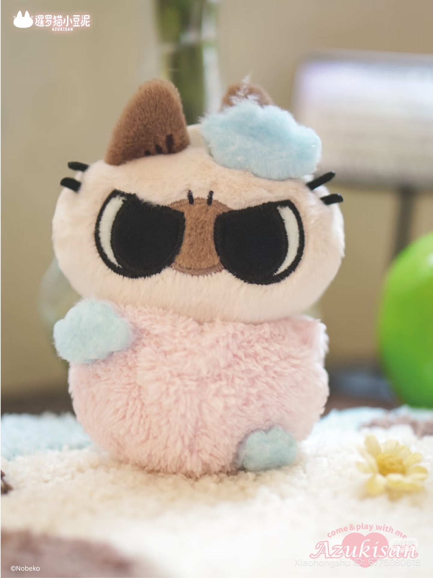 Azukisan's Daily Life Series plush pendant, a grumpy cat toy with pastel pink fur and cloud appliqués, sitting beside a daisy. Preorder for Q4 2025.