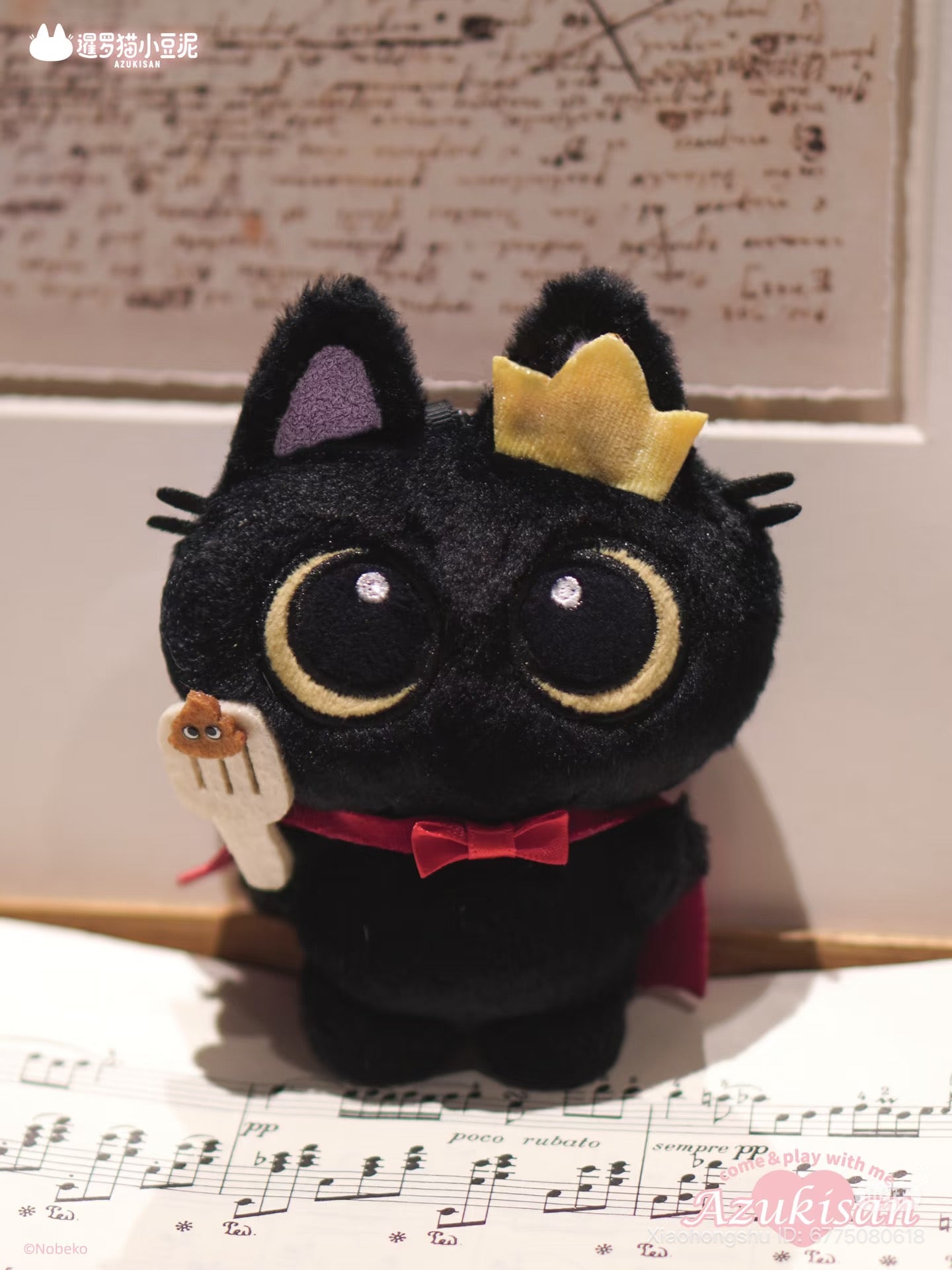Azukisan's Daily Life Series plush pendant, featuring a black cat toy with crown, bow tie, and fork, set on sheet music.