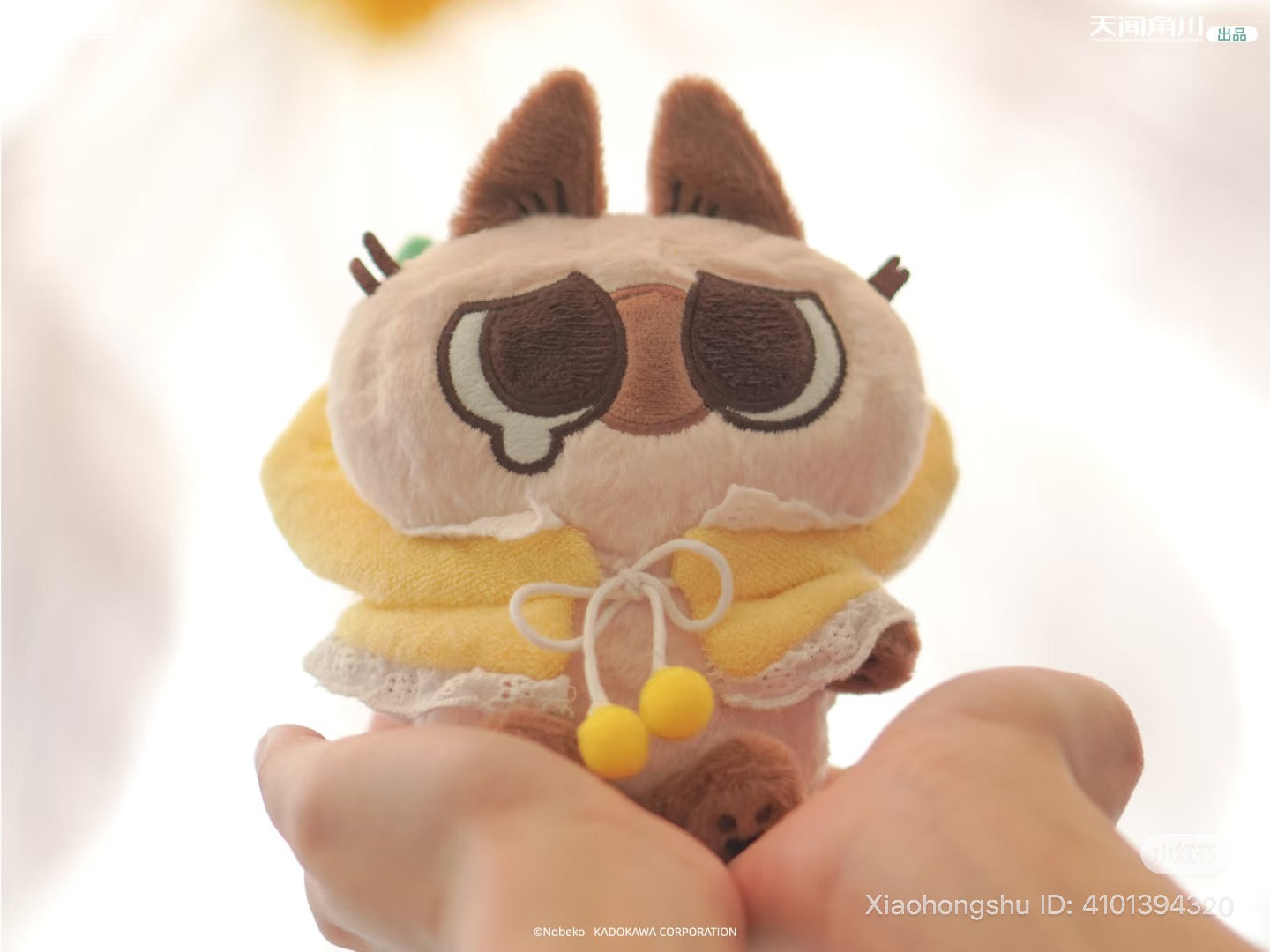 Small plush toy from Azukisan-Fruity series, featuring oversized eyes, a yellow hooded cape, and pom-pom ties, held in hands; part of a blind box collection.