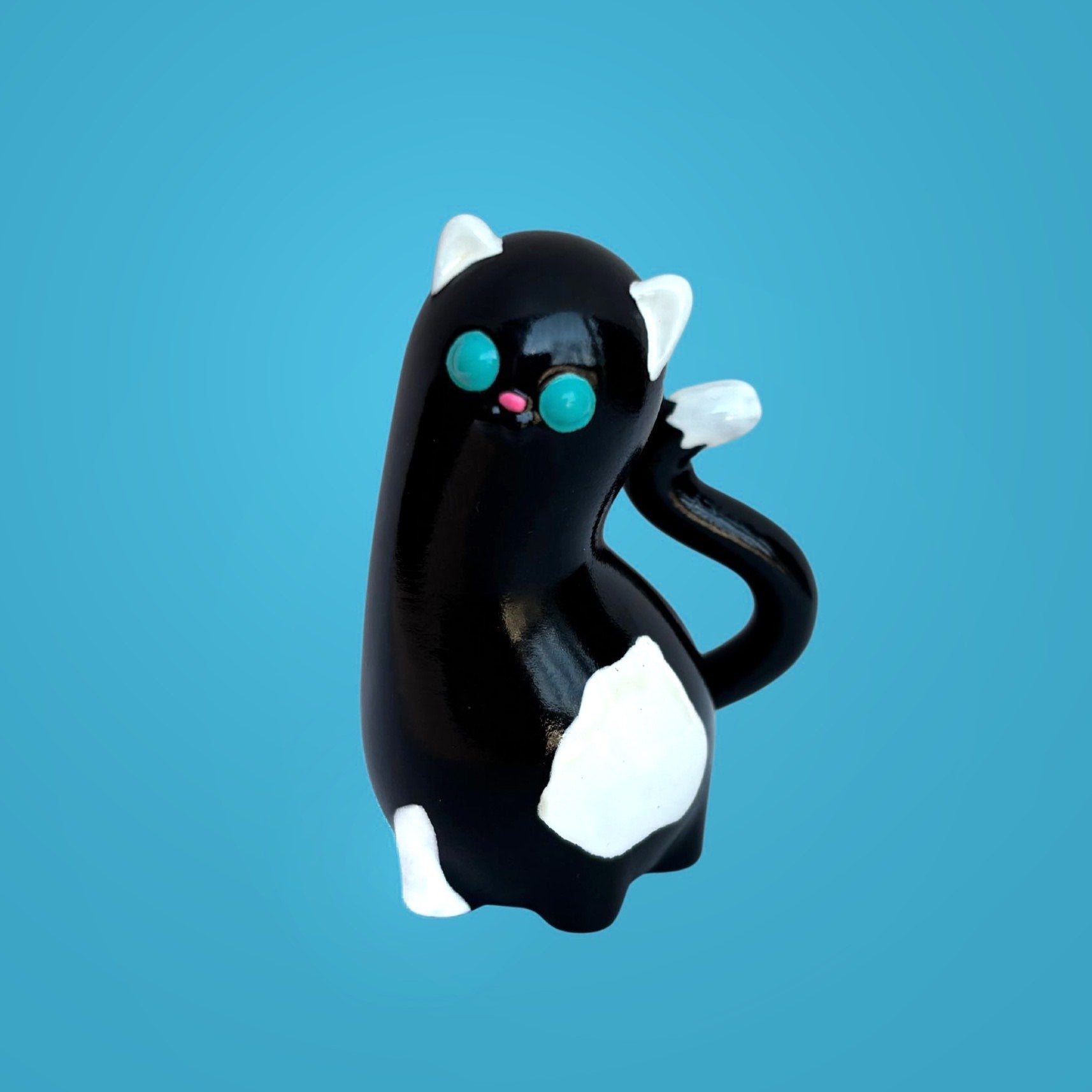 Spencer by Ghost Fox Toys: A glossy black resin cat figurine with white patches, teal eyes, and a pink nose, exhibiting artistic charm.