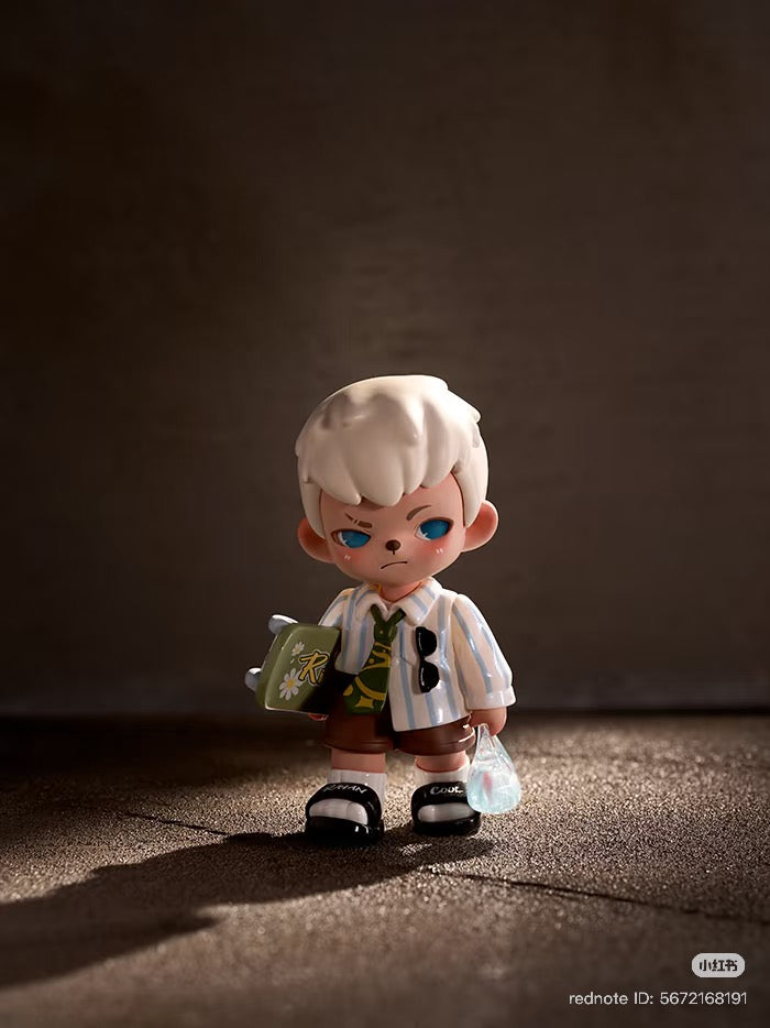 Chibi-style boy figure from Rayan Let't Date Series Blind Box, with white hair, preppy outfit, holding a book and shopping bag. Preorder for Q4 2025.