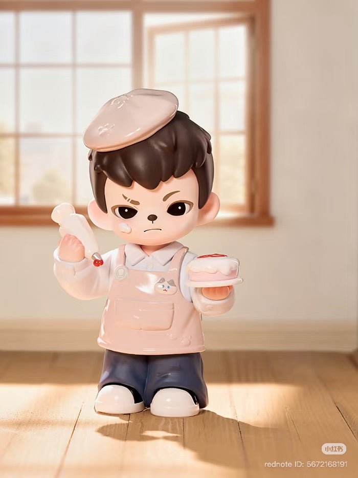 Rayan Let't Date Series figurine: boy in beret with piping bag and frosted cake, poised on sunlit floor. Preorder available at Strangecat Toys.