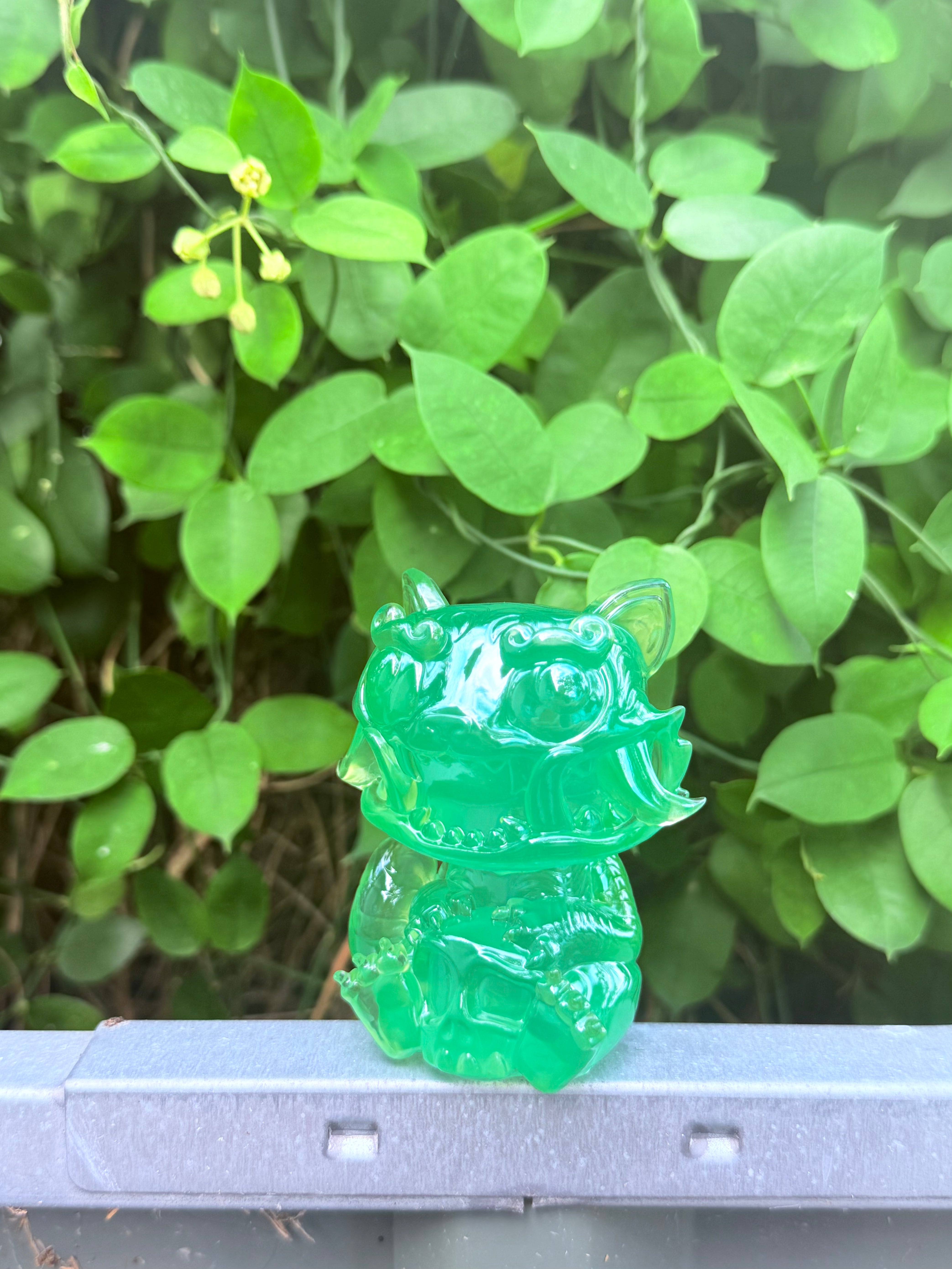 RuRu by Tomodachi Island: a small, translucent green resin figurine of a mythic beast with round eyes, a toothy grin, and curled horns, perched on a ledge.