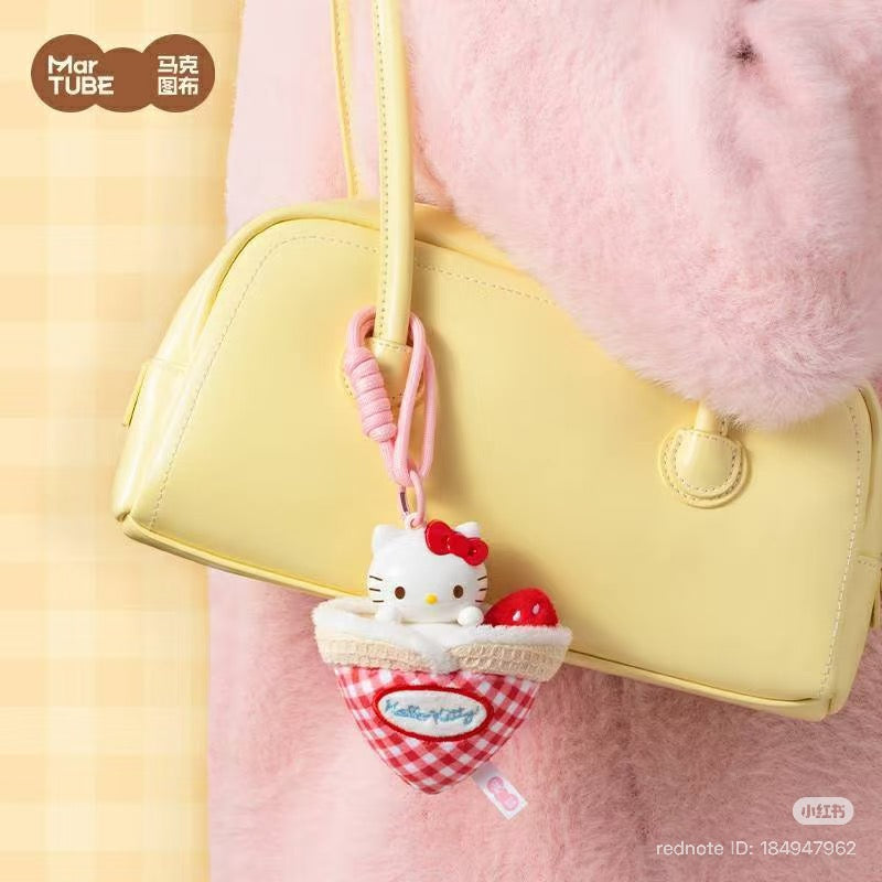 Pale-yellow handbag with Hello Kitty Afternoon Tea Scented Blind Box Keychain, featuring Hello Kitty in a gingham pocket with a strawberry, attached by pink lanyard.