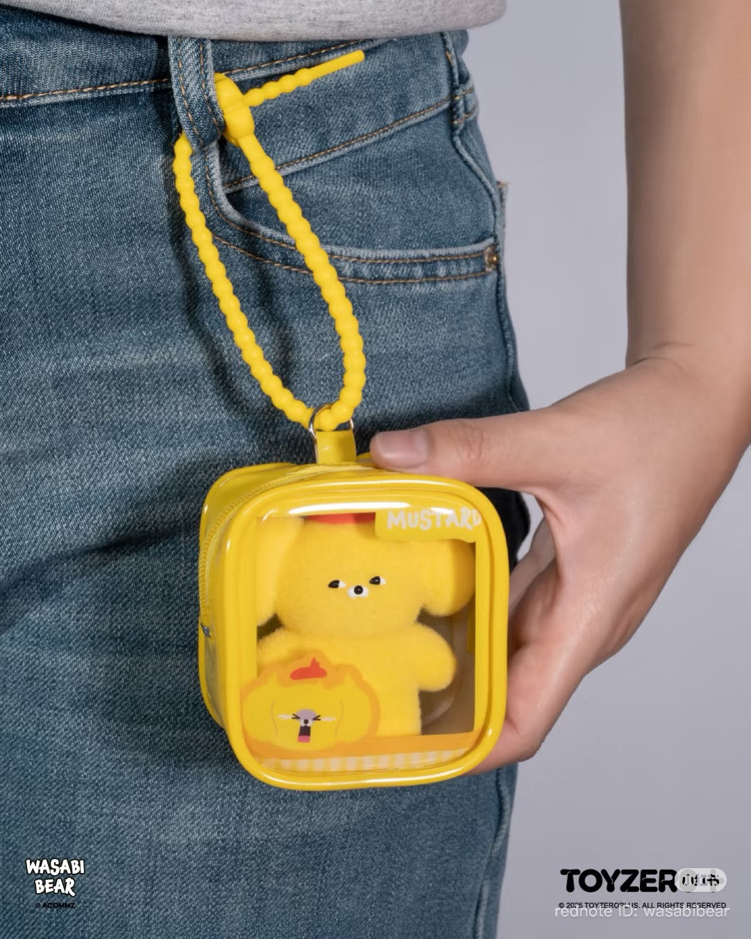 Wasabi Bear Outing Pals Series Blind Box: Small yellow pouch with a mustard bear figurine, held against jeans. Preorder for Strangecat Toys' unique art toy collection.