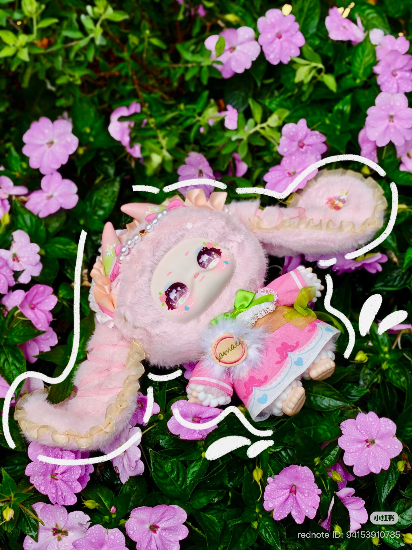 Samael Misty Garden plush doll on pink flowers, featuring a mask-like face, sparkly eyes, fluffy braids, and frilly pastel outfit. Part of a 400% plush series.