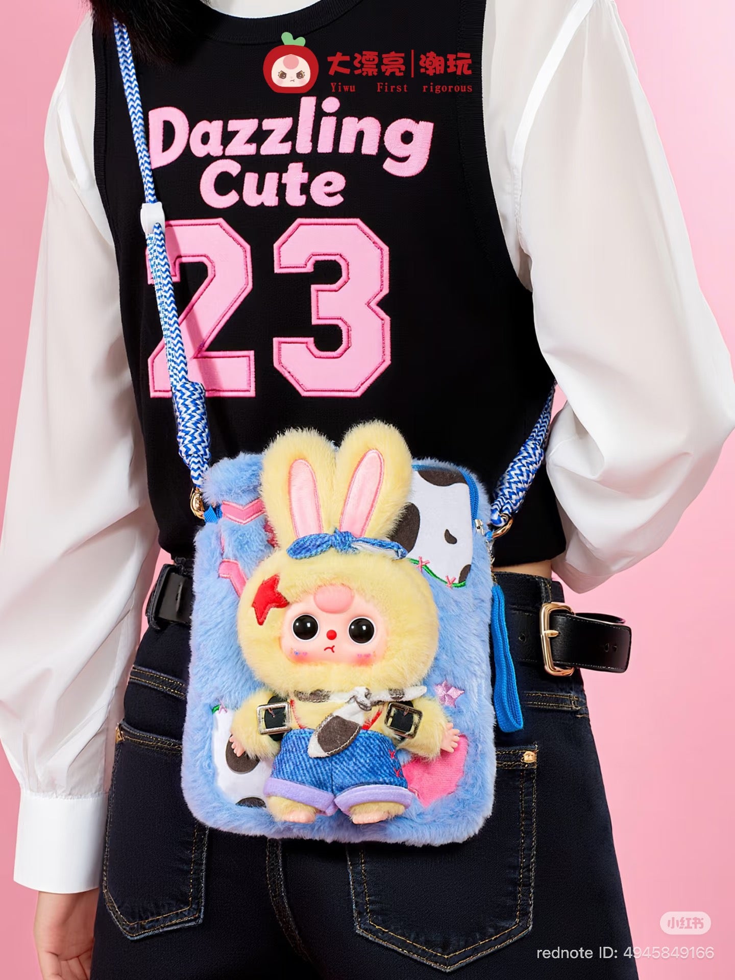 Back view of a person wearing a Baby Three Plush Travel Bag, featuring a plush bunny character with denim overalls and a braided strap.