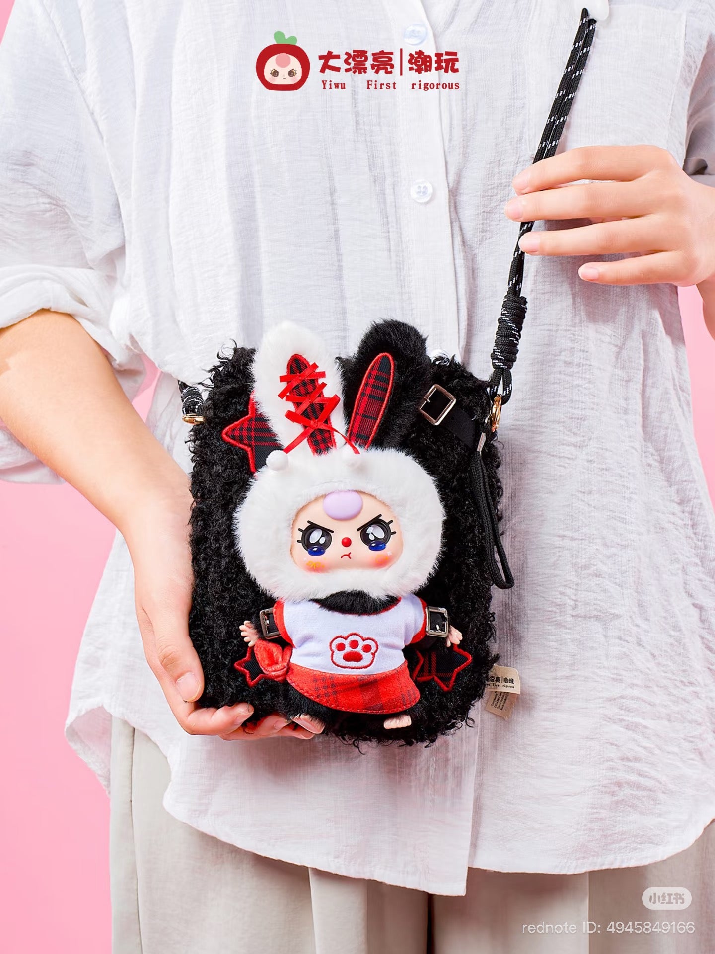 Person holding a Baby Three Plush Travel Bag with a black faux fur design, featuring a stylized plush doll in a plaid outfit and bunny ears.
