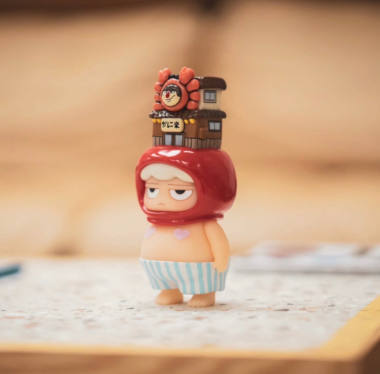 Poh x Worldsman vinyl figure: a grumpy character in striped shorts with a crab-themed restaurant helmet, reflecting Strangecat Toys' unique designer toy offerings.
