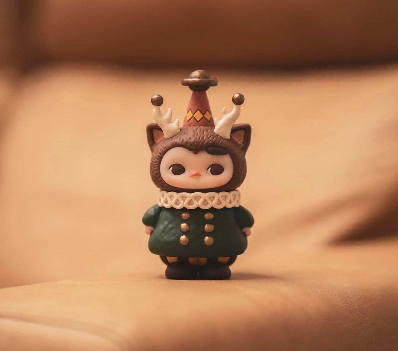 Pucky x Kaori Morris Pucky figurine: whimsical creature in green coat, fuzzy hood with cat ears, antler-like protrusions, and party hat. Preorder for Jan 2026.
