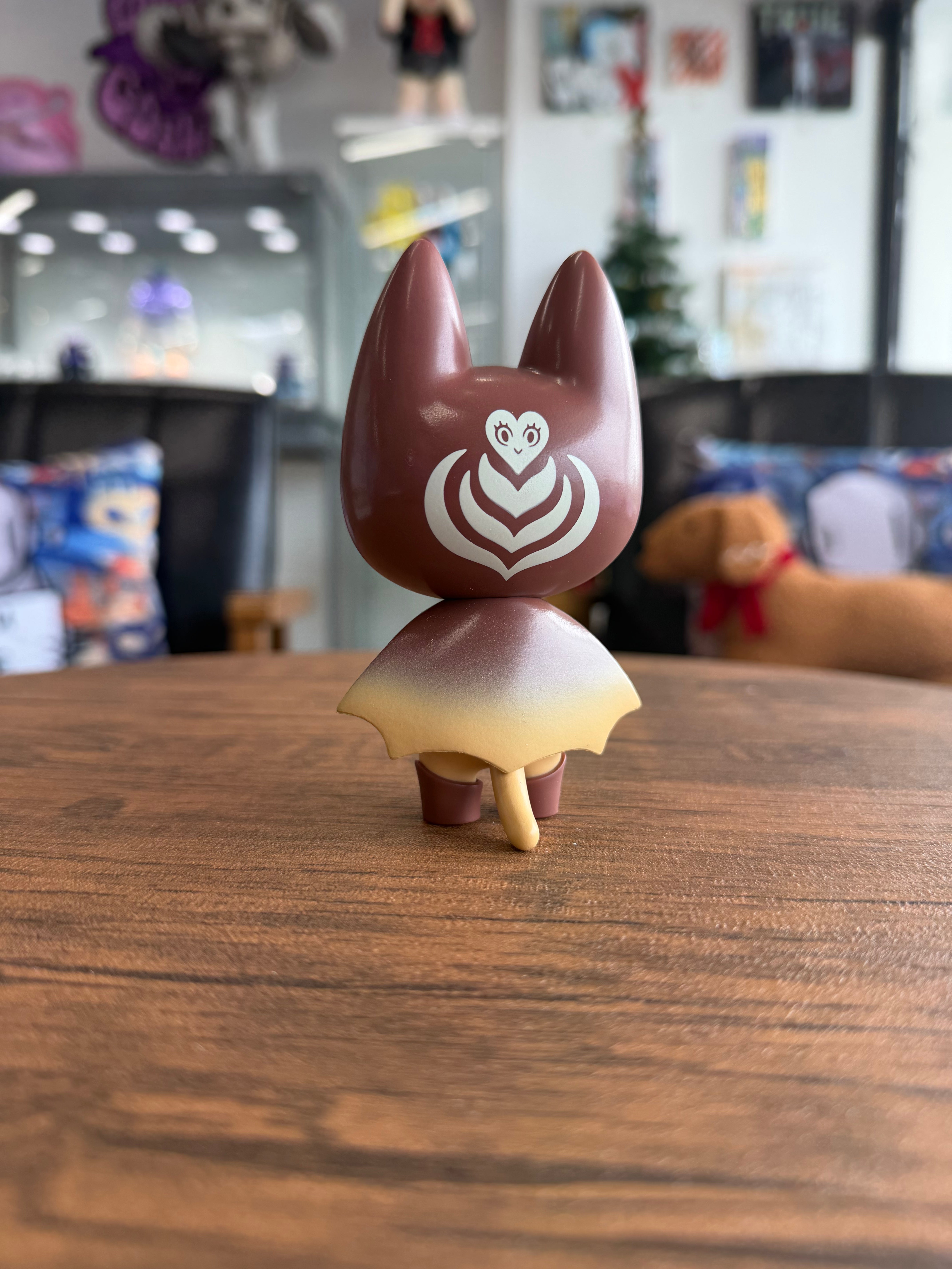 BAD MEAW 'Latte' EDITION by MUEANFUN SAPANAKE: 4 vinyl toy with cat ears, heart-and-chevron motif, flared skirt, and tail, displayed in a shop setting.