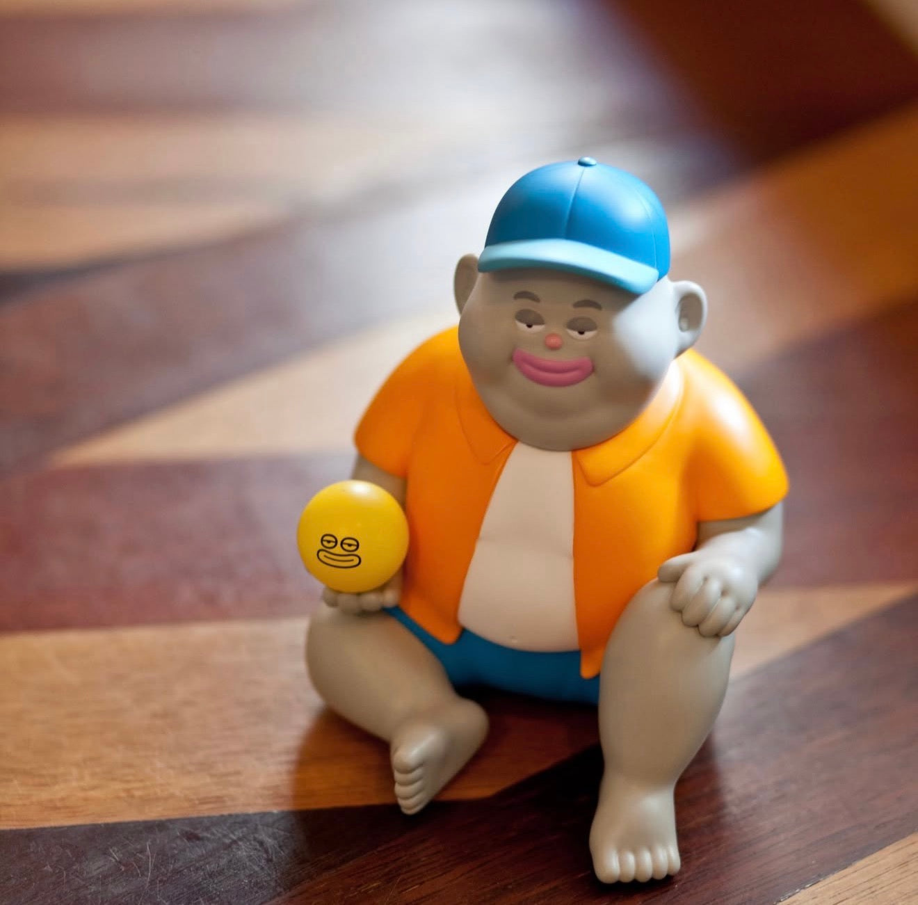 Miller by Jim Dreams: A 13.5cm vinyl figurine with a cartoonish expression, seated, wearing casual clothes, holding a yellow ball with a similar face.