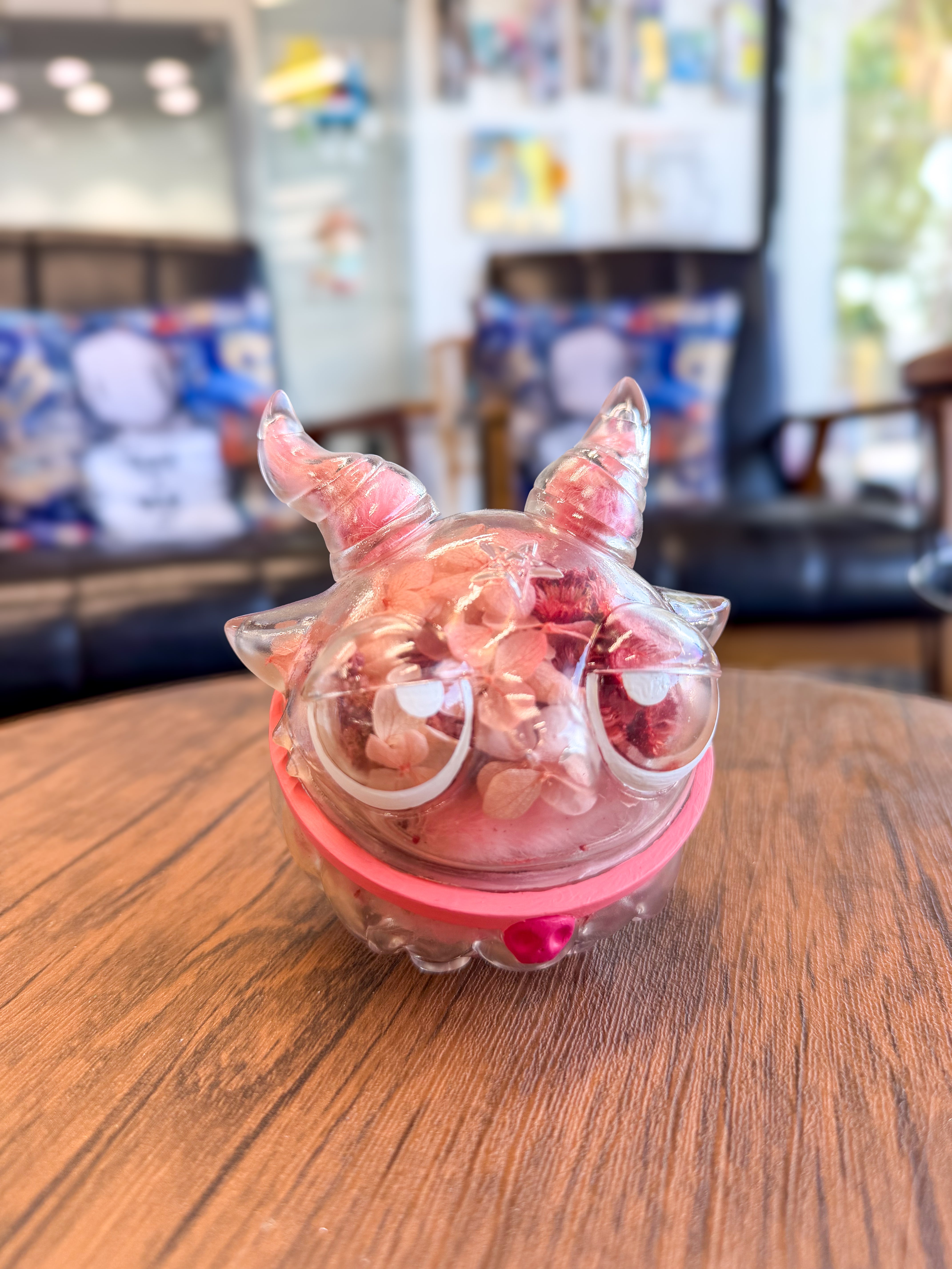Sweet on the inside Bobbi by Zintears: A 10cm transparent vinyl creature with pinkish dried flowers, featuring oversized eyes and a pink band, displayed on a tabletop.