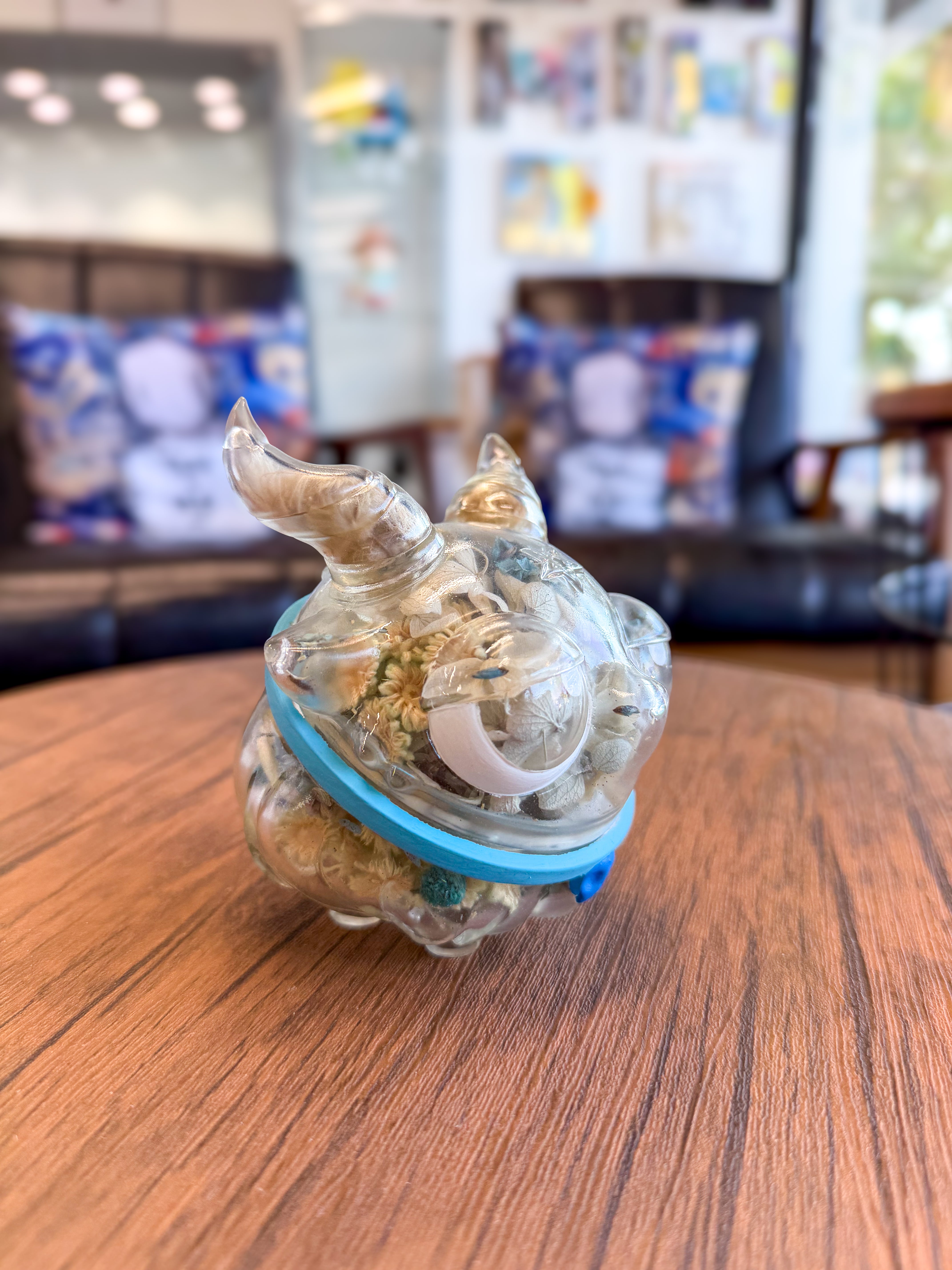Sweet on the inside Bobbi by Zintears: A vinyl pig-shaped container holding dried flowers, secured with a blue band, on a wooden tabletop.