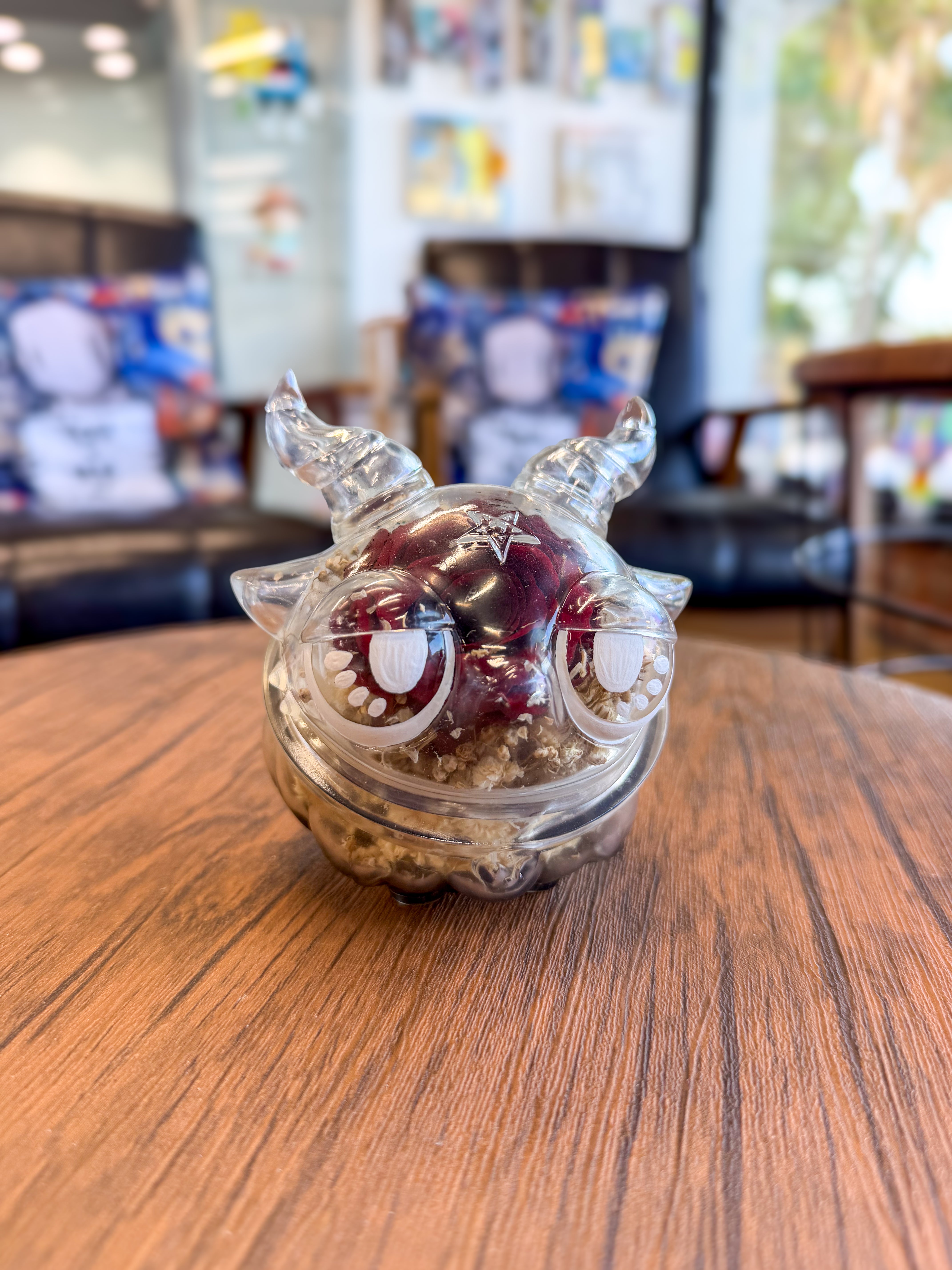 Sweet on the inside Bobbi by Zintears: A 10cm vinyl figurine with big eyes, horned head filled with dried petals, on a wooden table.