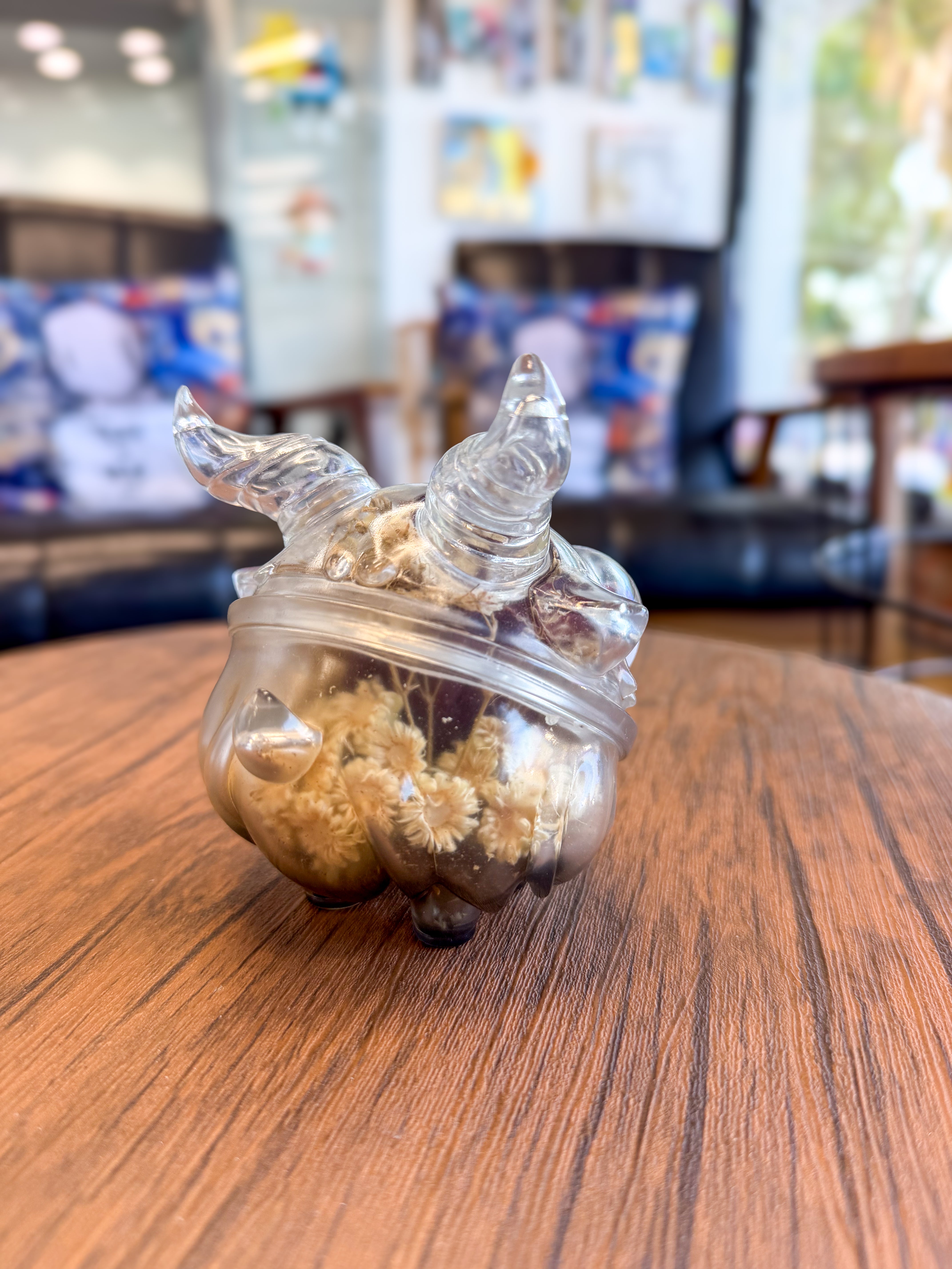 Sweet on the inside Bobbi by Zintears: A 10cm translucent, horned creature-shaped vinyl jar, showcasing dried daisy-like blossoms, on a wooden tabletop.