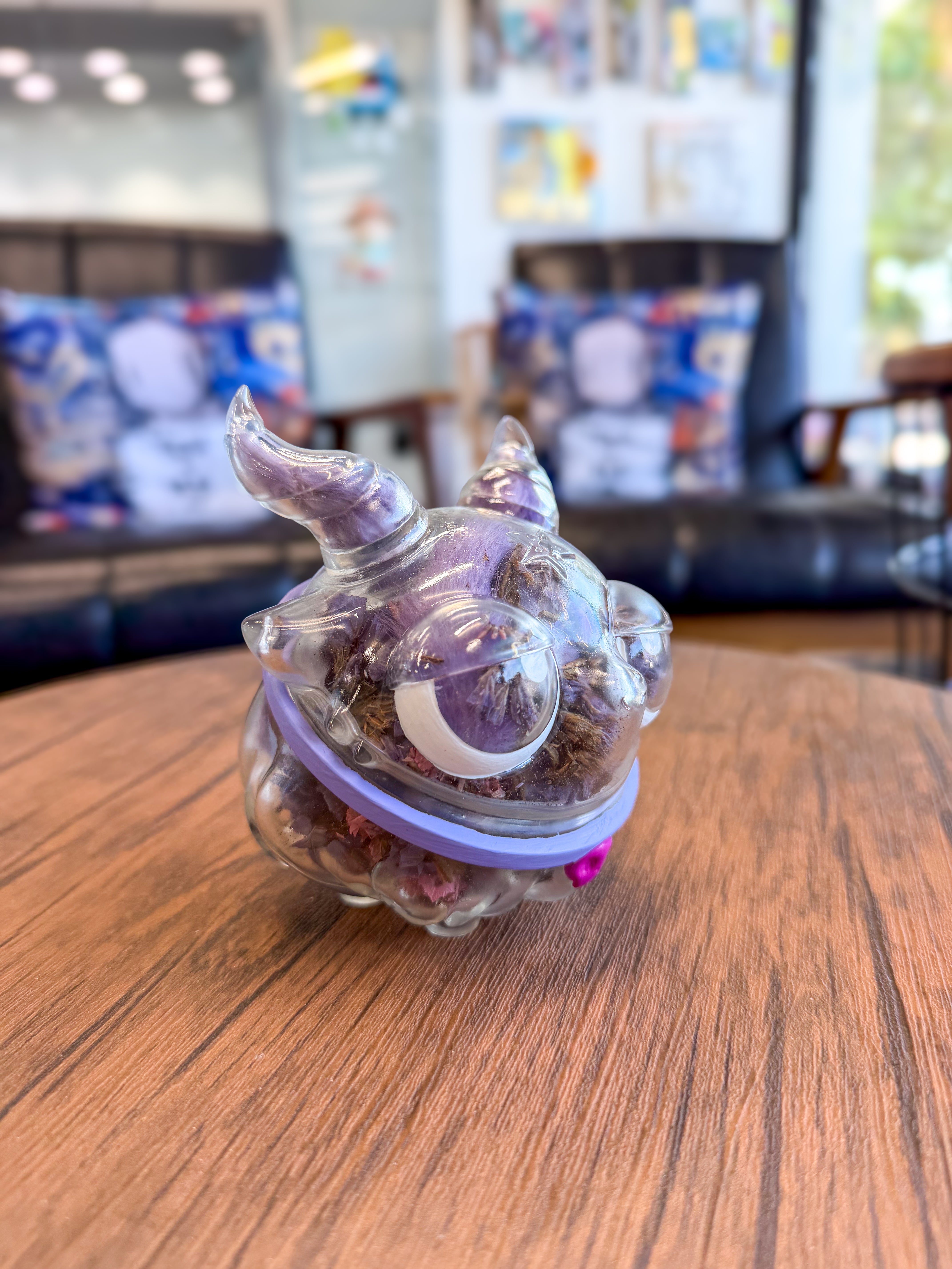 Sweet on the inside Bobbi by Zintears, a 10cm clear vinyl monster figurine holding dried petals, displayed on a wooden table in a cozy setting.