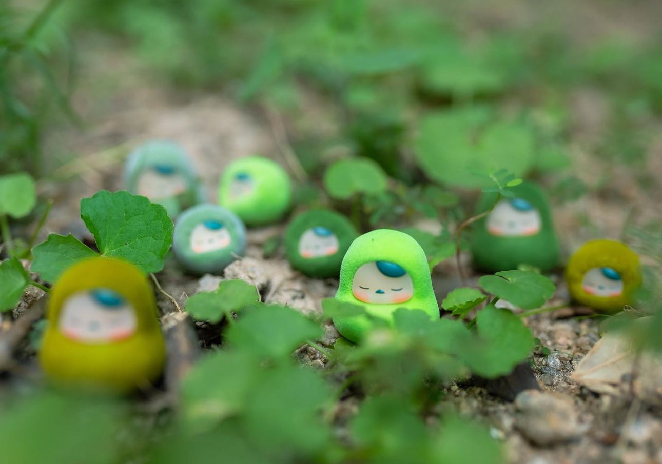 Moss Beanie by Pucky vinyl toy with terrarium accessories in dirt with small toys, green ball, toy face, and leaf close-ups.