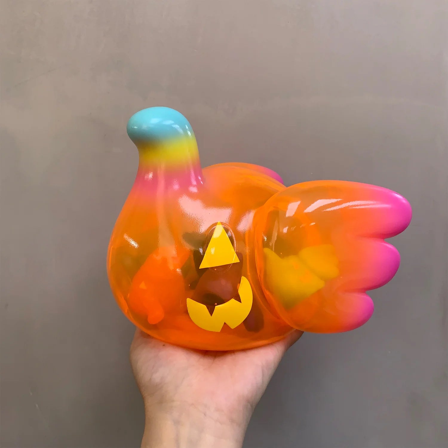 Hand holding Elfie Pumpkin Head Edition toy, a translucent, bird-shaped squishy with jack-o-lantern face. Preorder for November 2025 release.