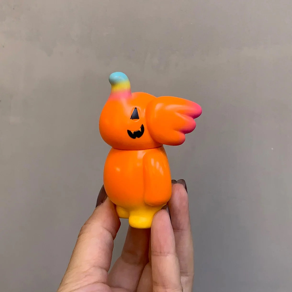 Elfie Here I Am! 100% Pumpkin Edition vinyl art-toy, orange creature with a jack-o-lantern face, single wing-like ear, glossy finish, 3 inches tall.