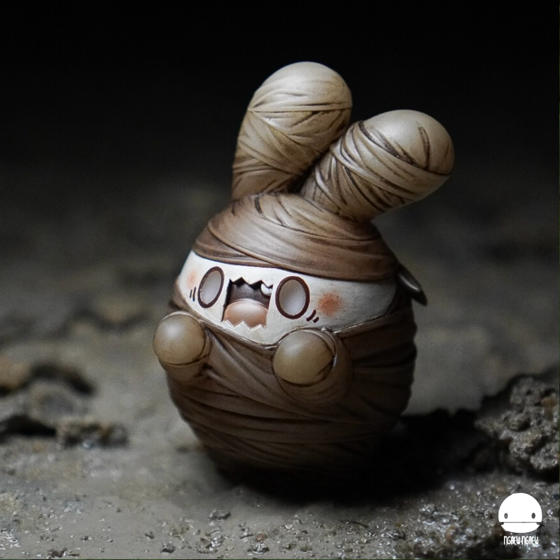 Ngaew Ngaew Mummy by Ngaew, a spherical resin art toy with bandage details and bunny ears, stands on a dirt-like surface; limited to 70 pieces.