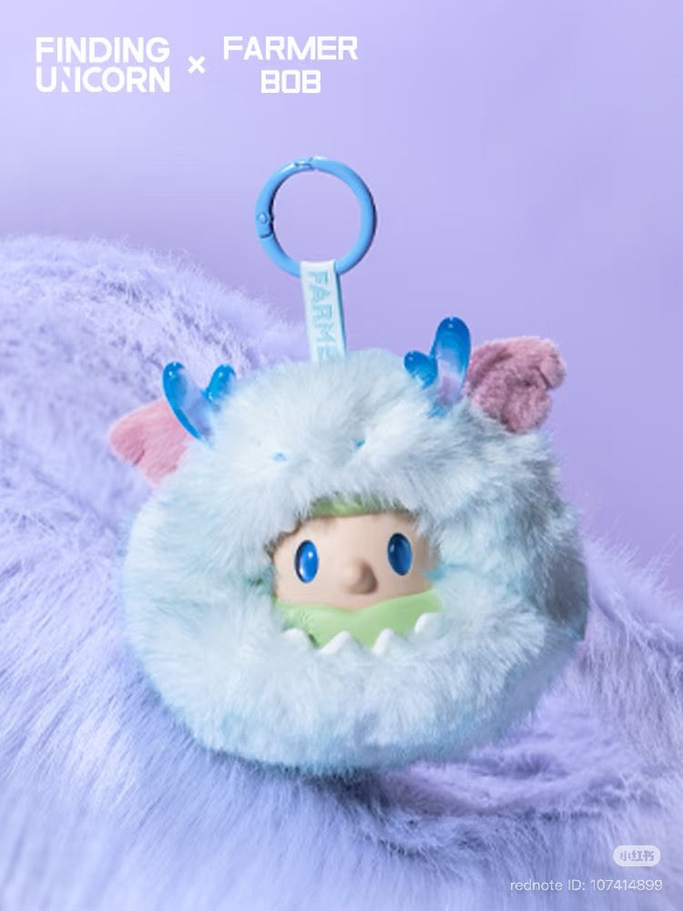 FARMER BOB Mini - DRAGON MIRAGE SERIES: Powder-blue faux-fur pom-pom charm with cartoon face, blue horns, and pink ears. Includes blue clip for bags or keys.