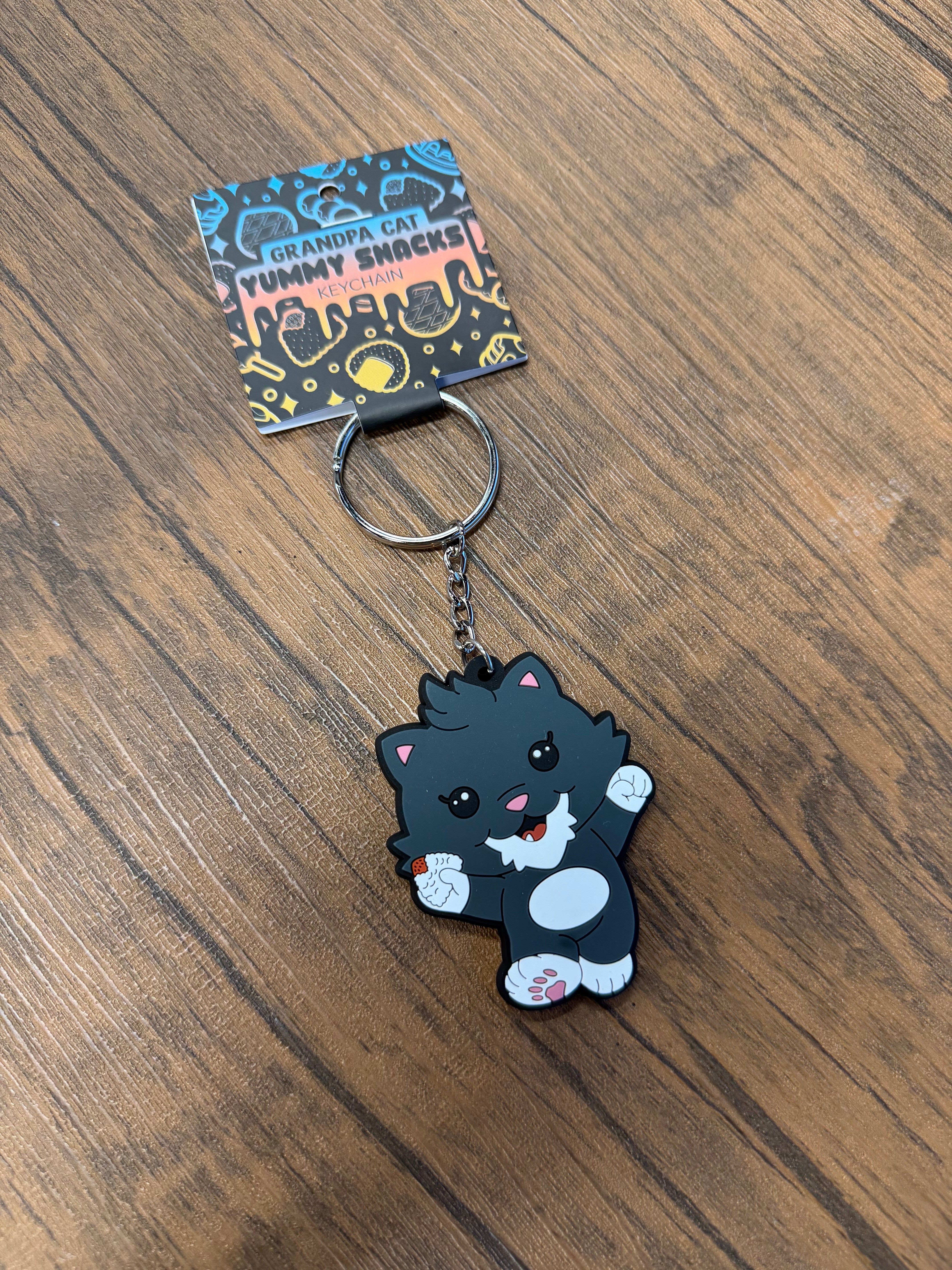 Chibi-style Grandpa Keychain - Japanese Snack Series featuring a happy cartoon cat with a rice-ball snack, on a display card with metal ring attachment.