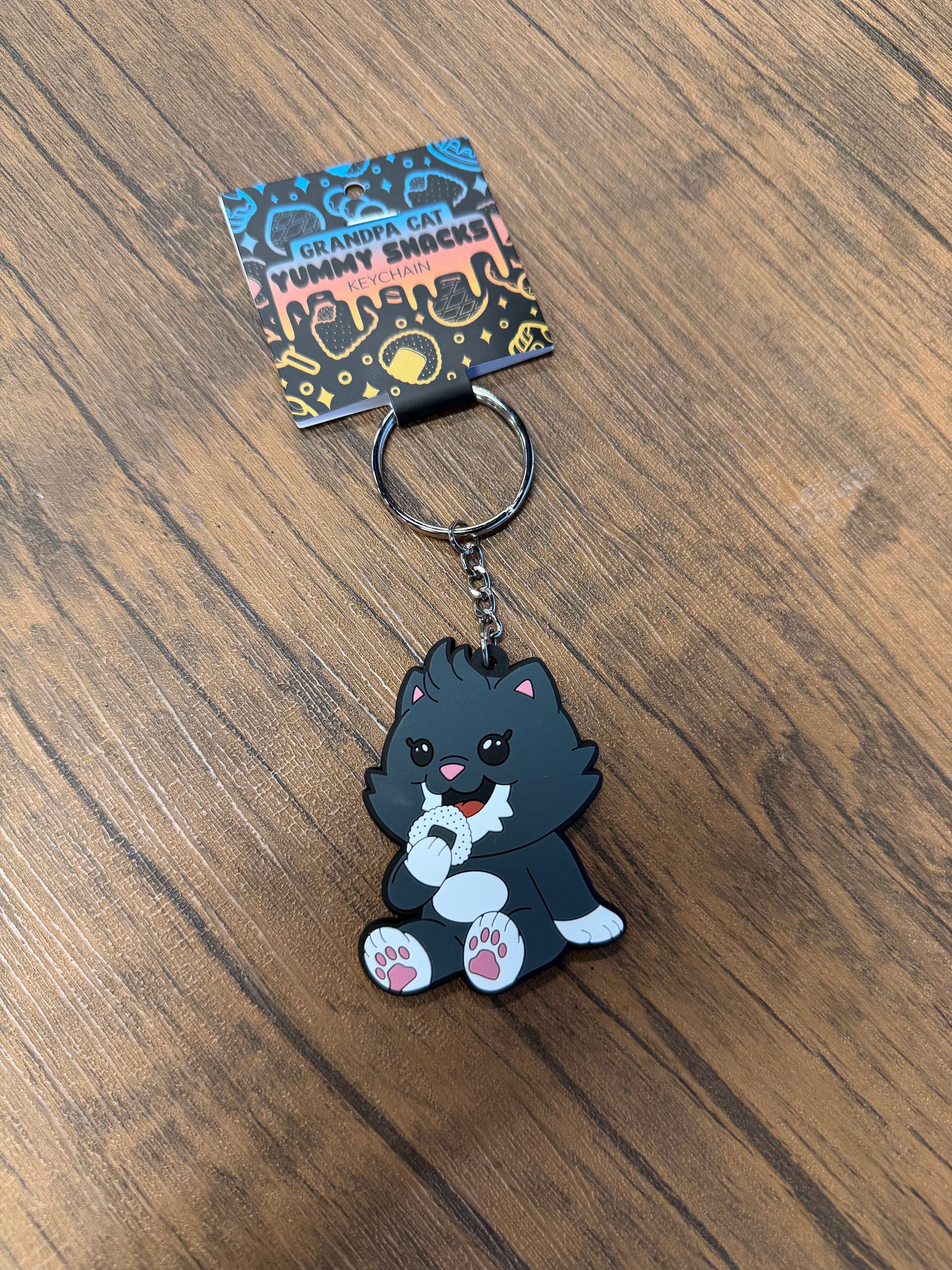 Grandpa Keychain - Japanese Snack Series features a cartoon cat charm enjoying a snack, packaged on a branded cardboard header, perfect for novelty collectors.