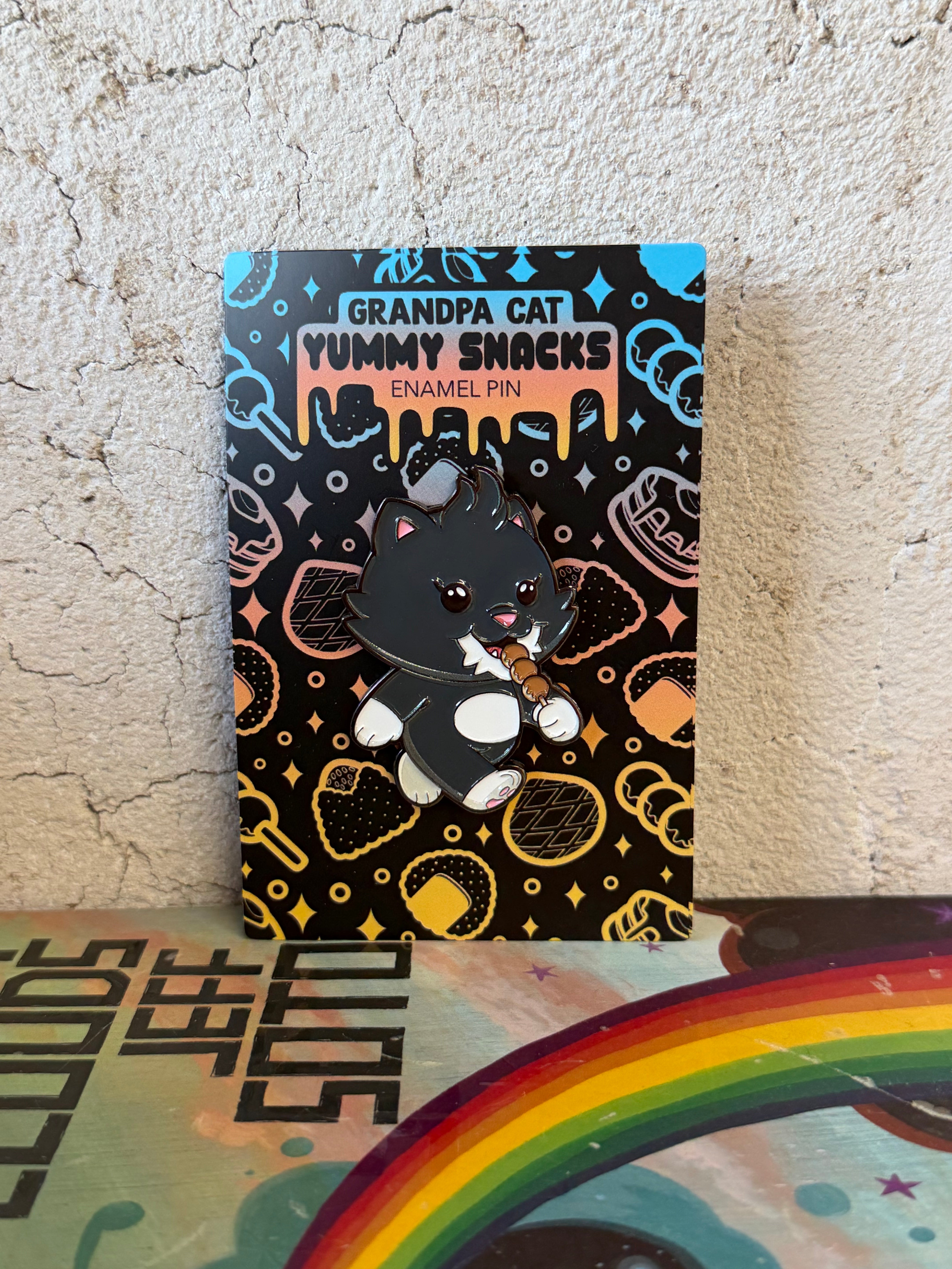 Grandpa Pin - Japanese Snack Series: A cartoon black cat enamel pin eating skewered snacks, mounted on a themed card with sweet treat silhouettes.