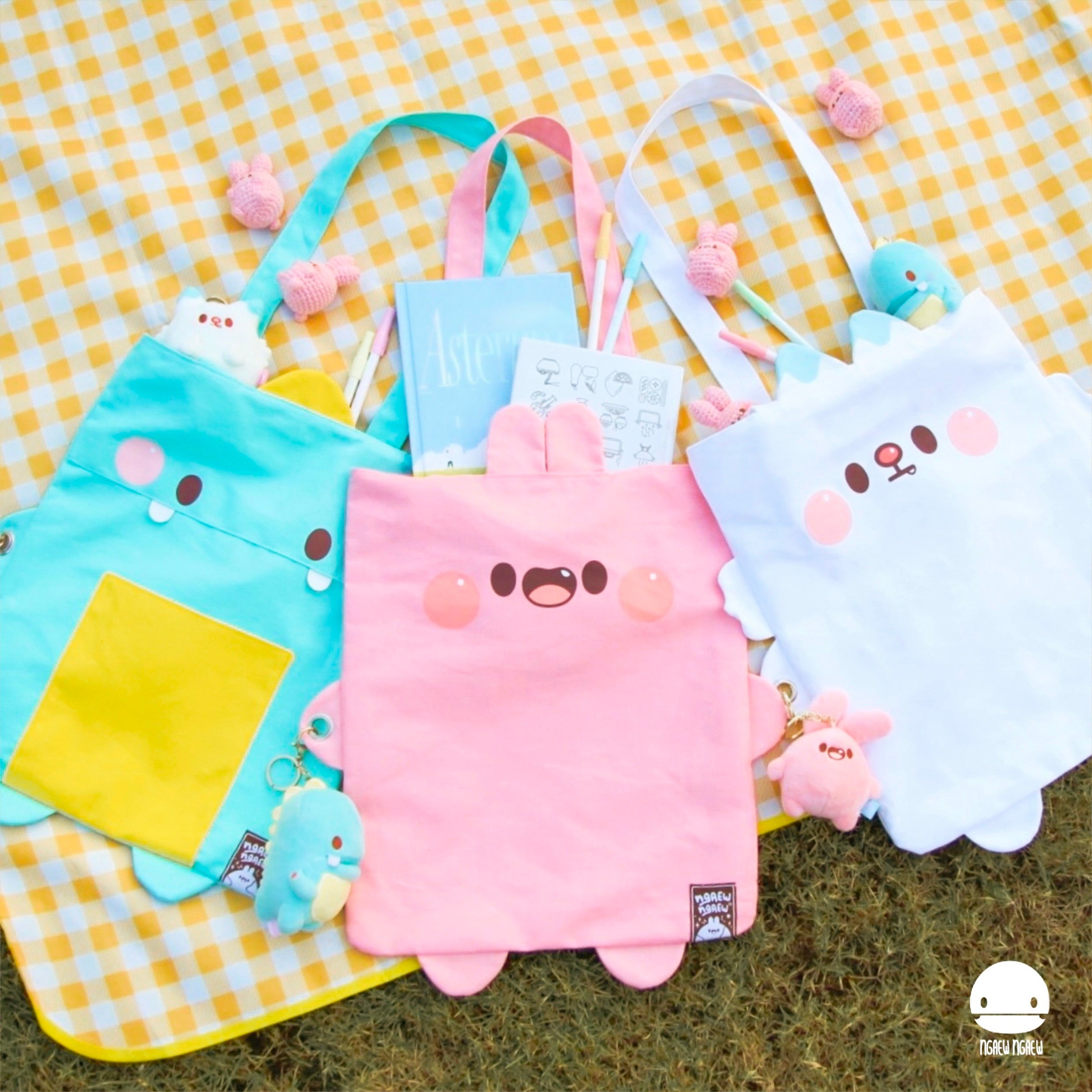 NGAEW NGAEW TOTE BAG set on blanket: mint-green, pink, and white bags featuring playful kawaii designs, plush keychains, and a pastel-themed interior.
