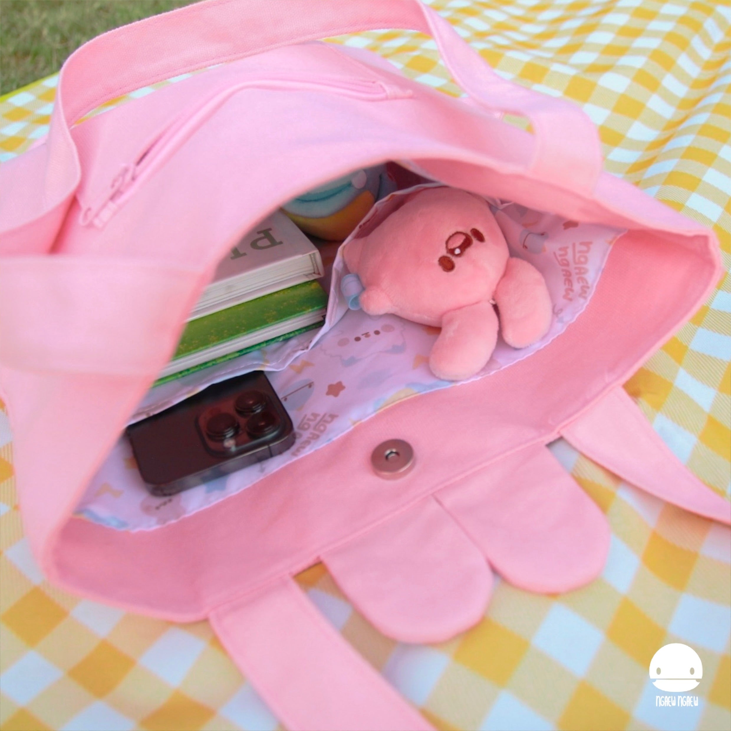 NGAEW NGAEW TOTE BAG on gingham blanket, open with plush toy, smartphone, books, and pastel ball inside, showcasing scalloped edge and magnetic snap closure.