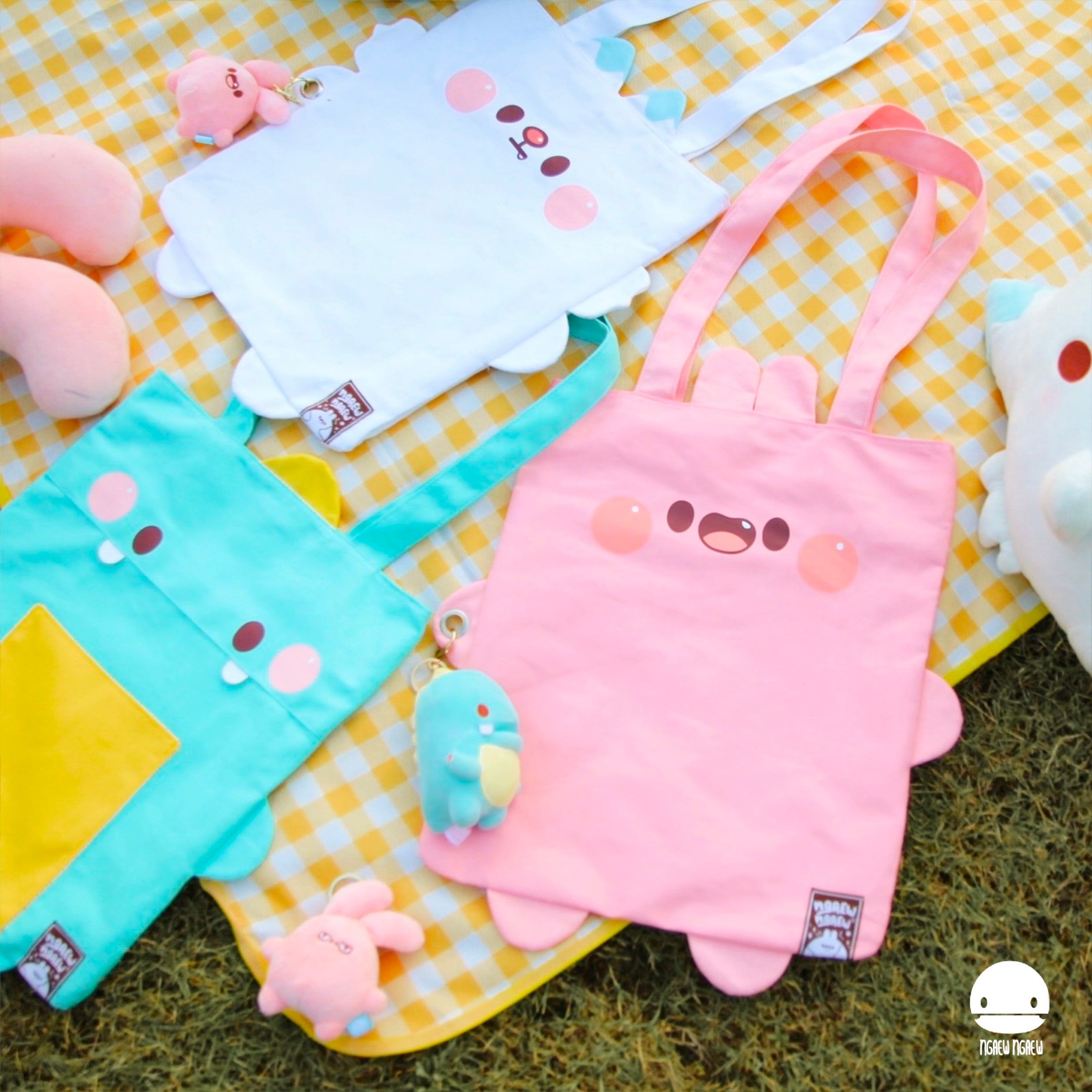 NGAEW NGAEW TOTE BAG flat-lay featuring three cartoon-faced tote bags with plush keychain toys on a picnic blanket, embodying Strangecat Toys' playful, artful style.