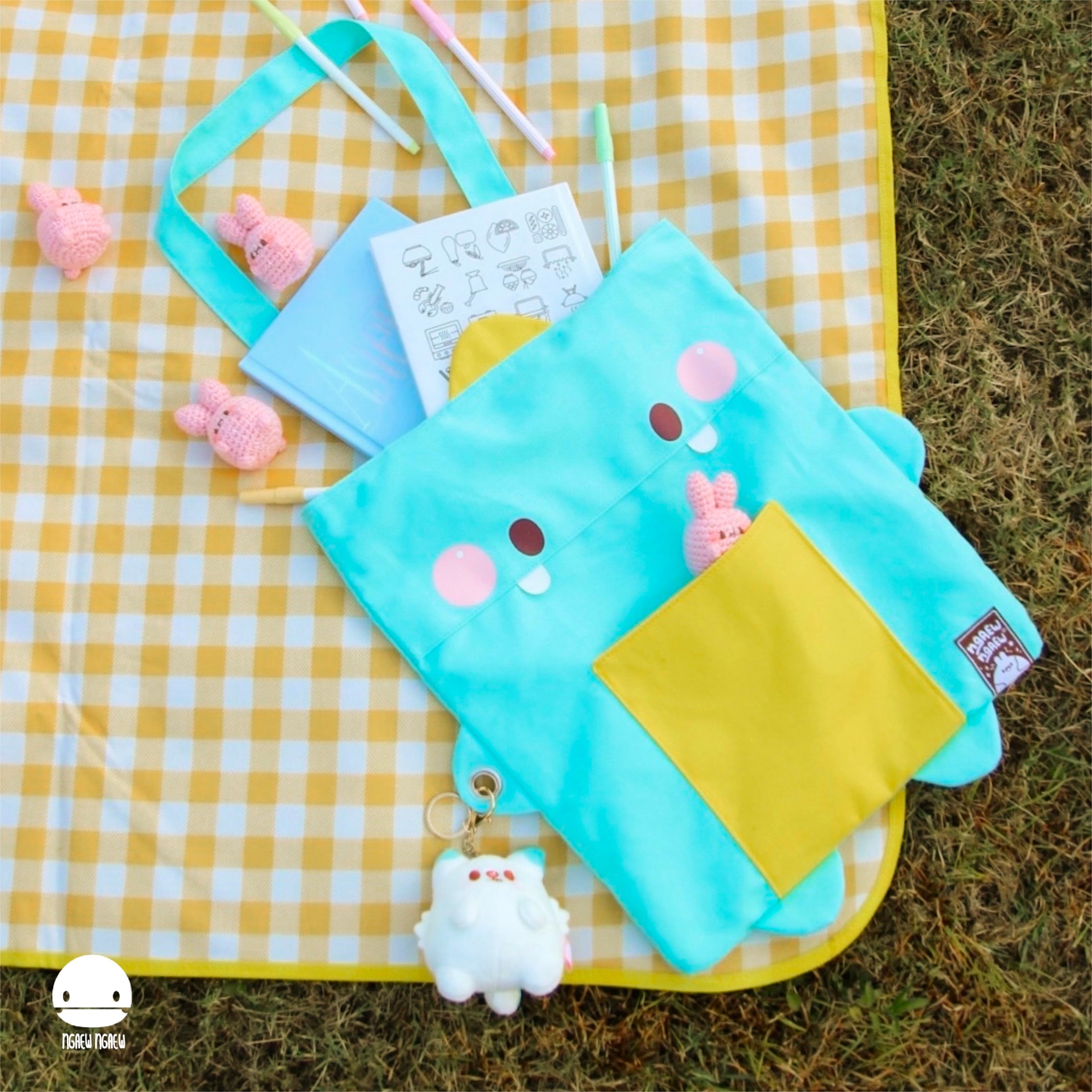 NGAEW NGAEW TOTE BAG displayed with notebooks, pastel pens, and pink crocheted bunnies on a picnic blanket, illustrating its playful, artistic vibe.