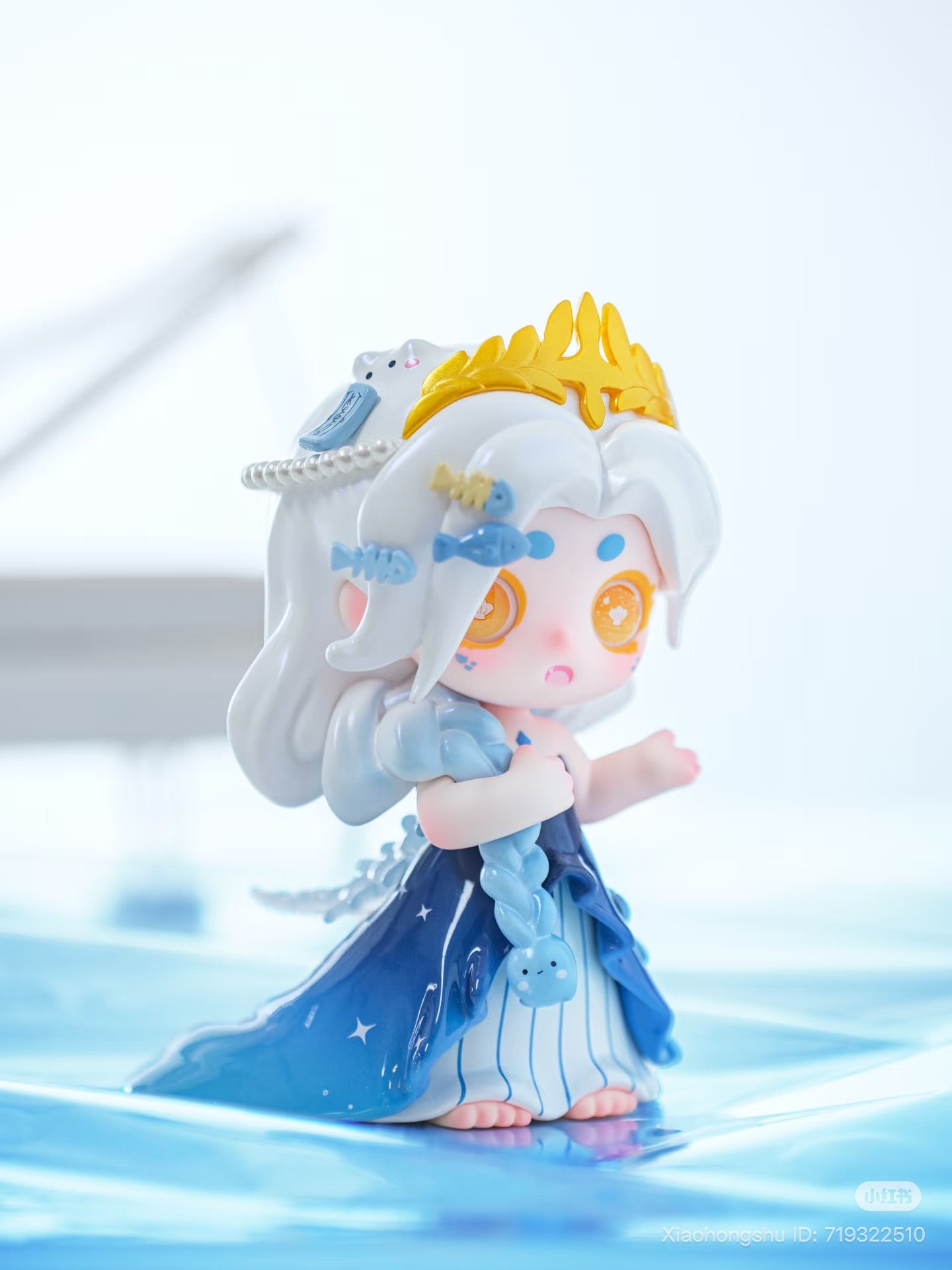 Keeno·Wish On The Sea Breeze Series Blind Box: Miniature sea-themed figure with white braided hair, gold crown, blue gown, and starry eyes, standing on a glossy surface.